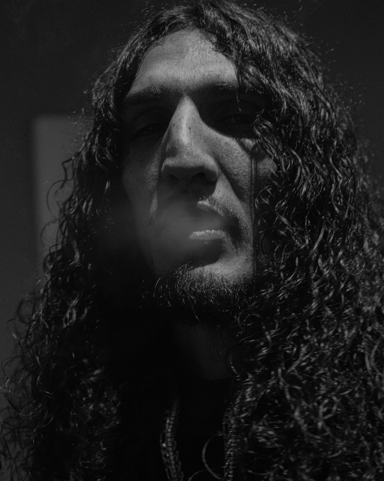 Black and white portrait of man with long curly hair and intense gaze.