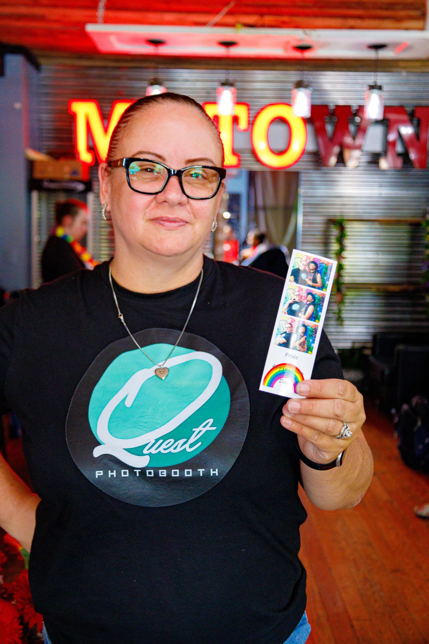 Woman holding photo booth strip smiling at Quest Photobooth event inside Motown-themed venue.