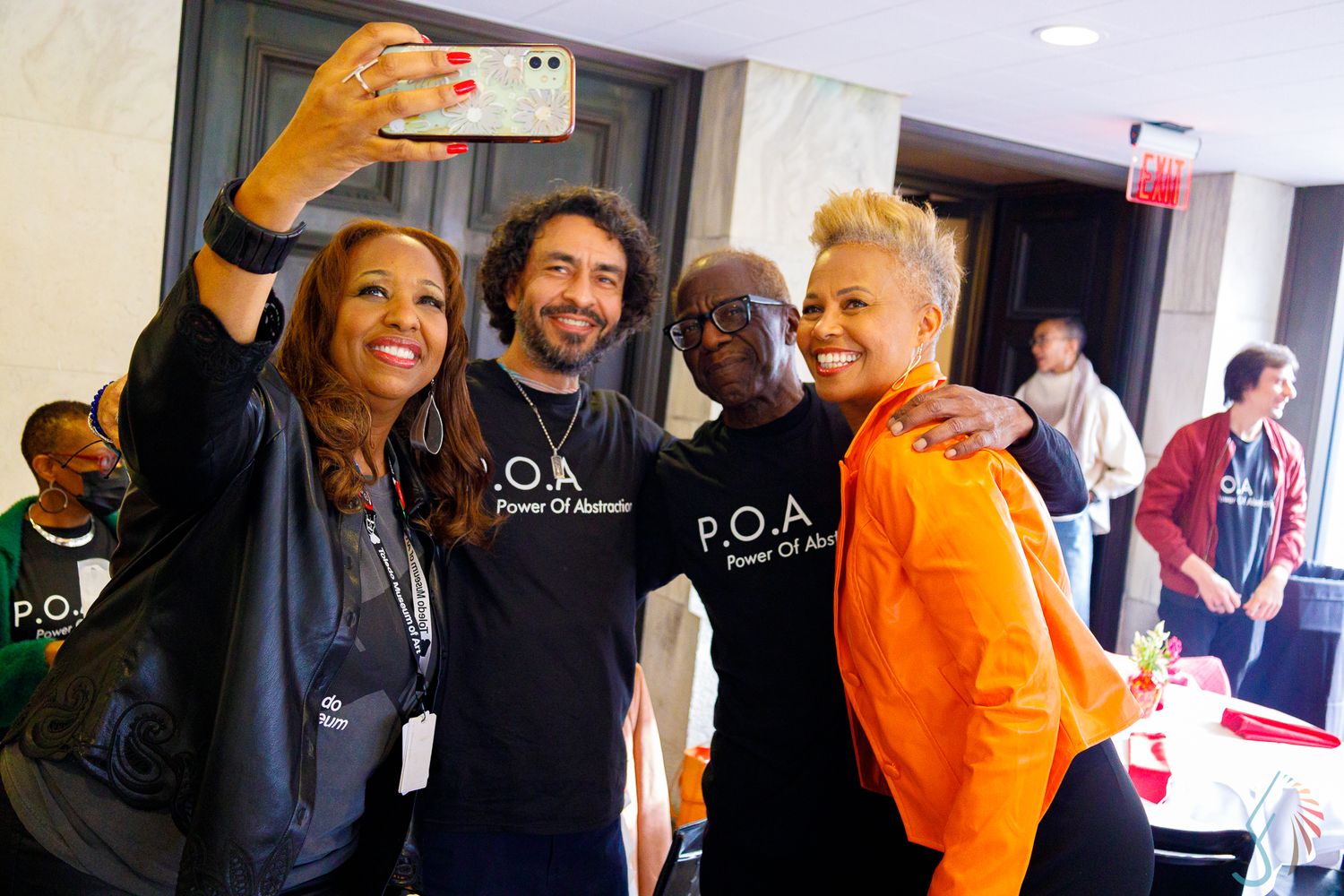 Four people pose for a selfie at a P.O.A. Power of Awesome networking event indoors.