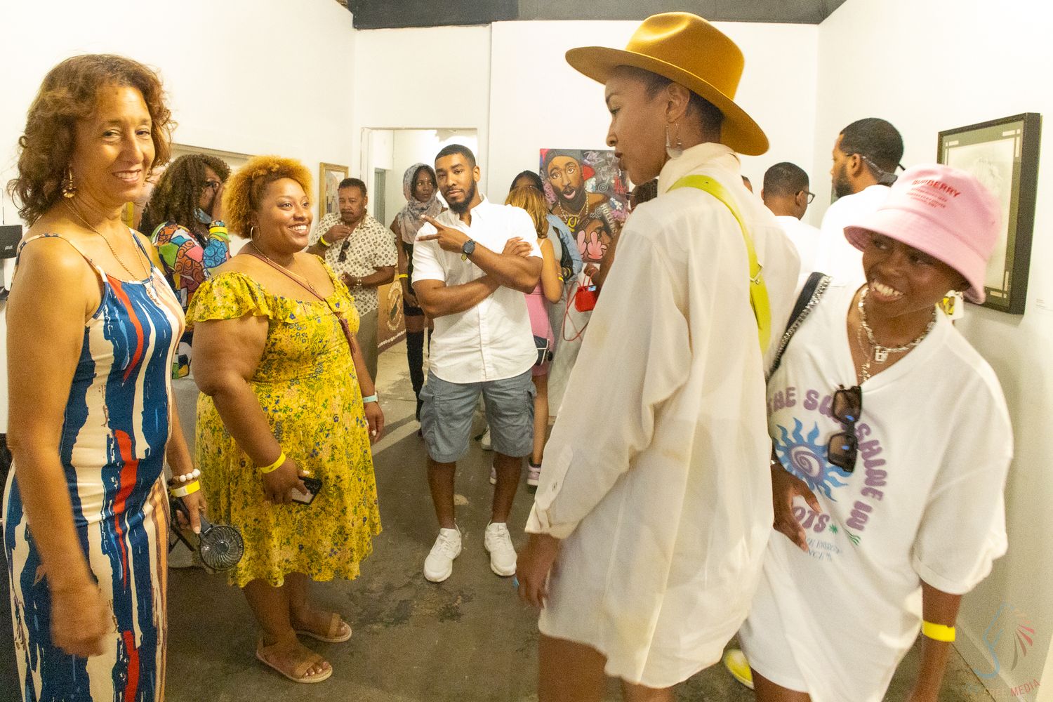 Diverse group of people socializing at an art gallery opening, wearing colorful summer outfits and stylish hats.