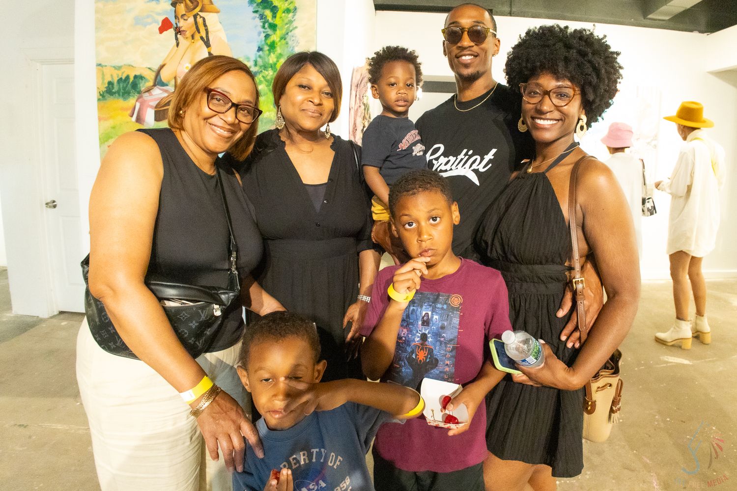 A joyful group of Black family members posing together at an art gallery event, including children and adults.