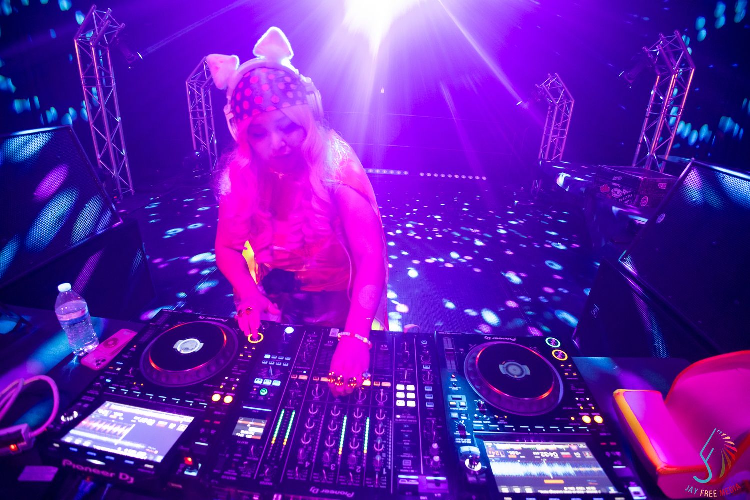 DJ performs under colorful purple stage lights at a nightclub event with professional equipment.