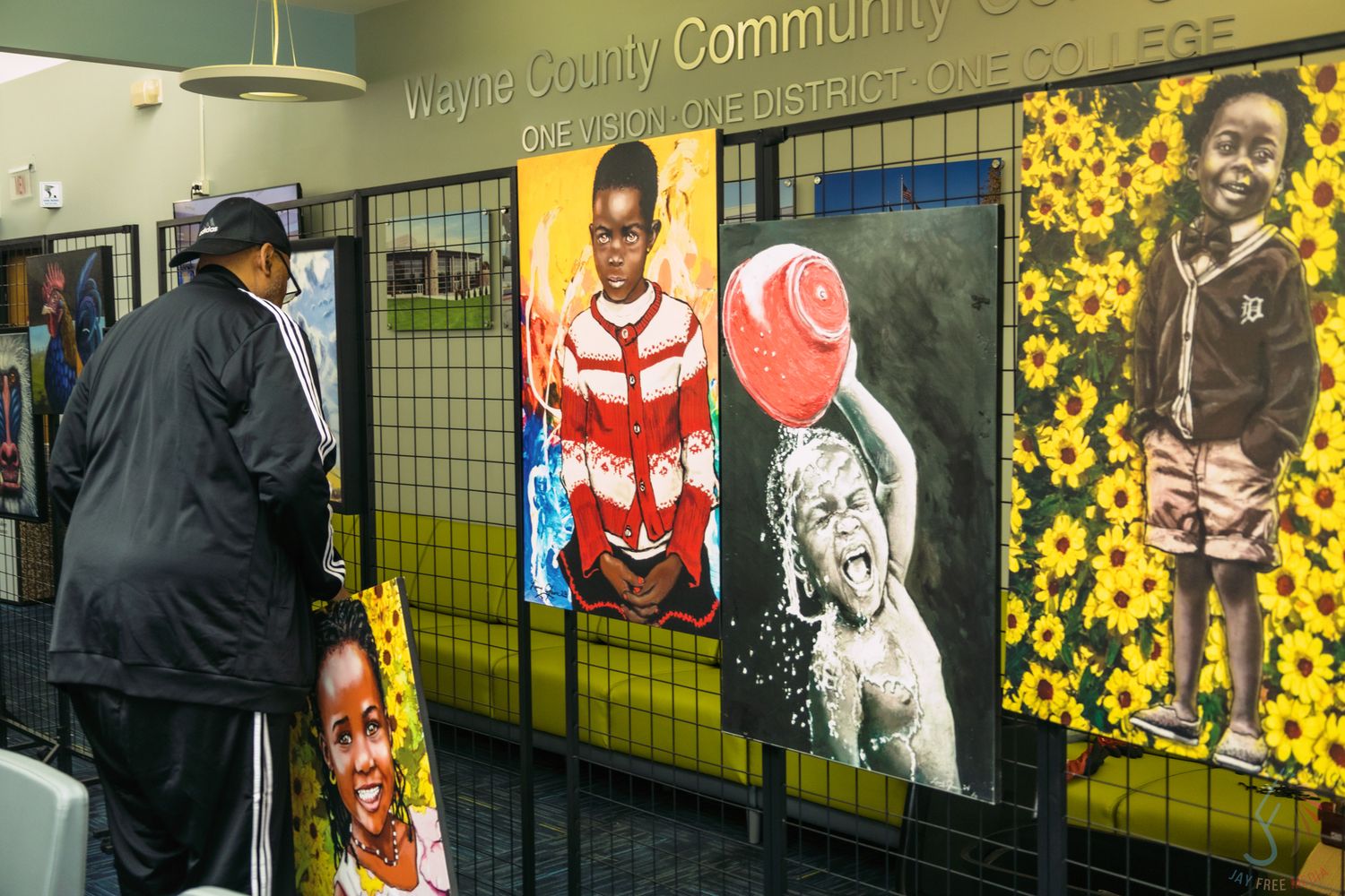 Person viewing colorful portrait artwork display at Wayne County Community College District gallery exhibition.