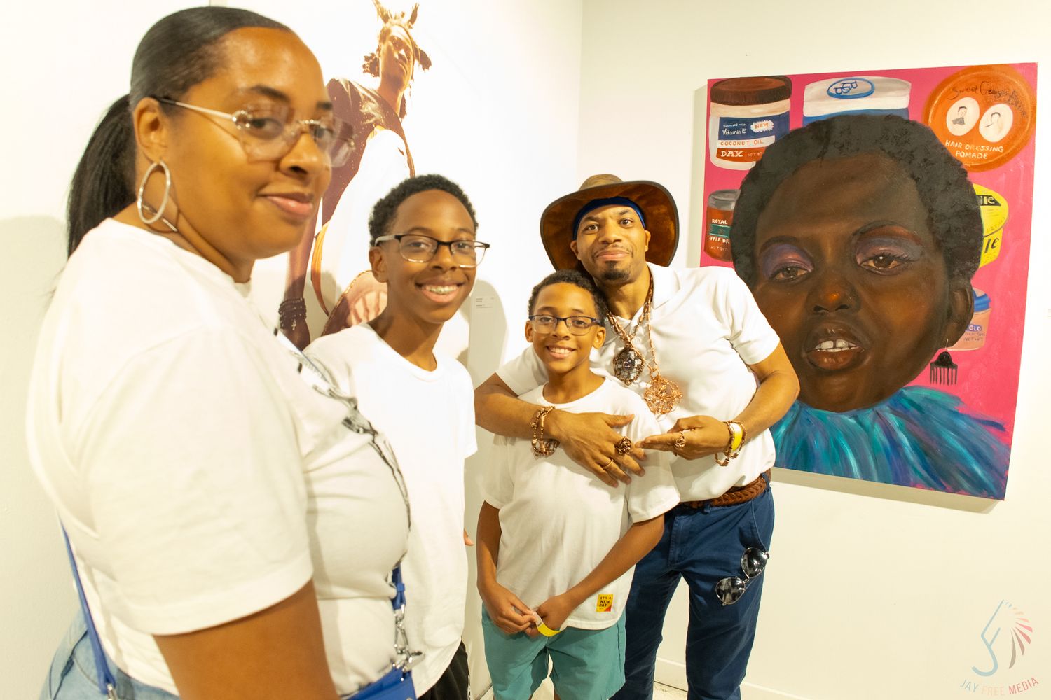 Four people smiling in an art gallery with colorful portrait paintings displayed on the wall behind them.