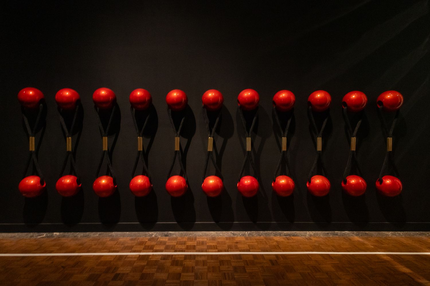 Row of red spheres mounted on wooden handles arranged in a grid pattern against a dark wall.