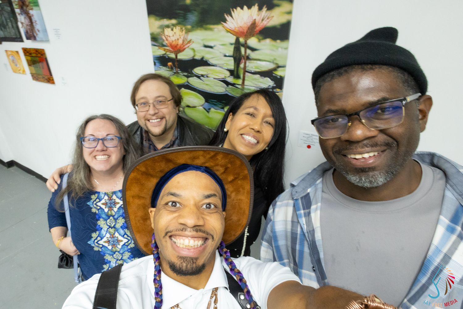 Five diverse friends smile together in a joyful group selfie in front of a floral painting.