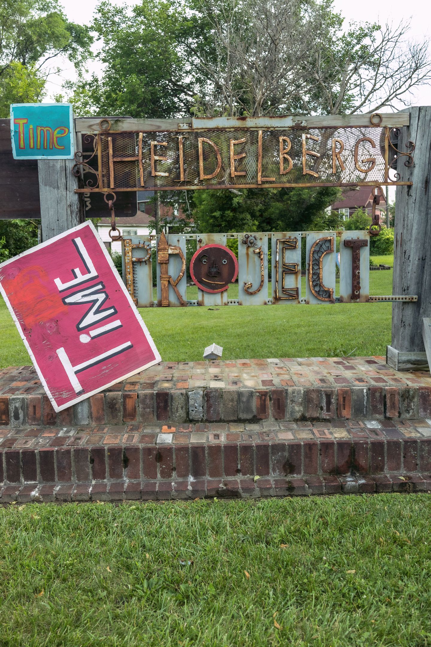 The Heidelberg Project outdoor art installation sign with a red Time sign on brick steps in Detroit, MI.