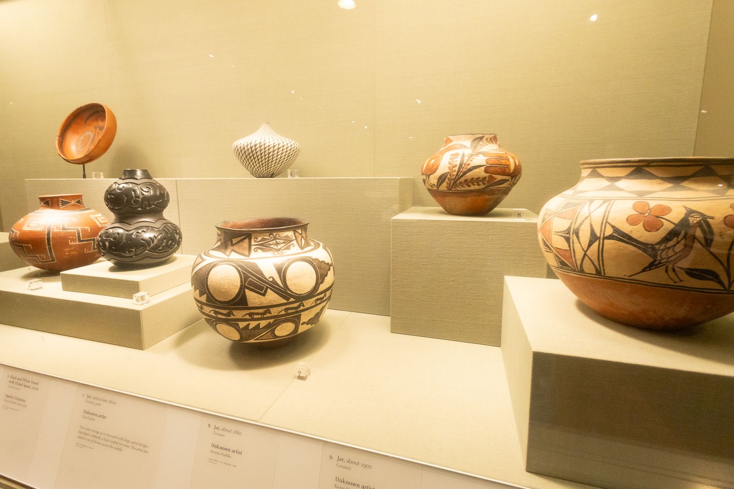 Museum display case showcasing Native American ceramic pottery with intricate geometric and floral designs on pedestals.