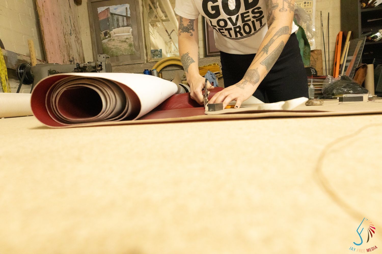Tattooed craftsman cutting large rolls of leather material on a workshop floor in Detroit.