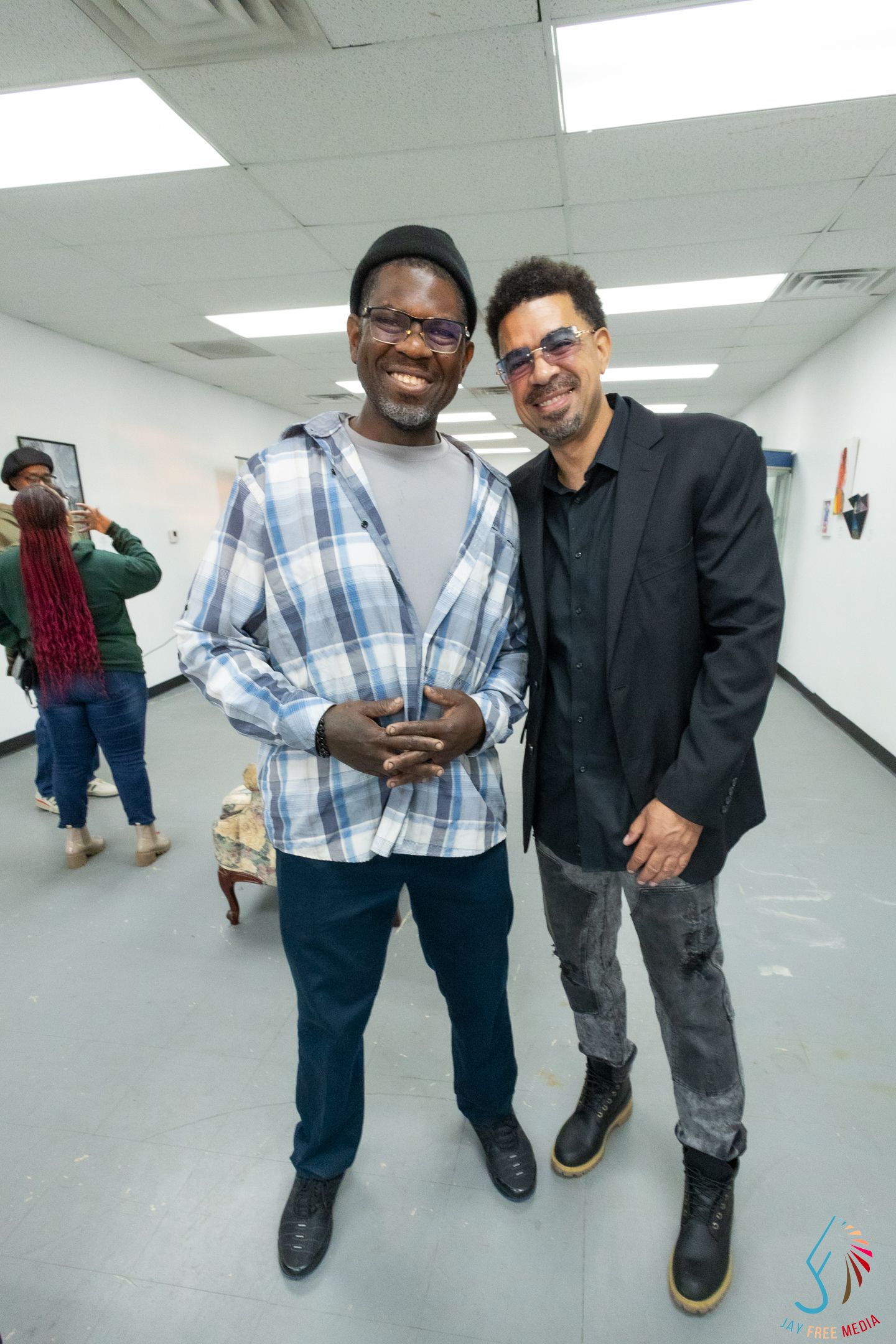 Two men smiling and posing together at an indoor art gallery event.
