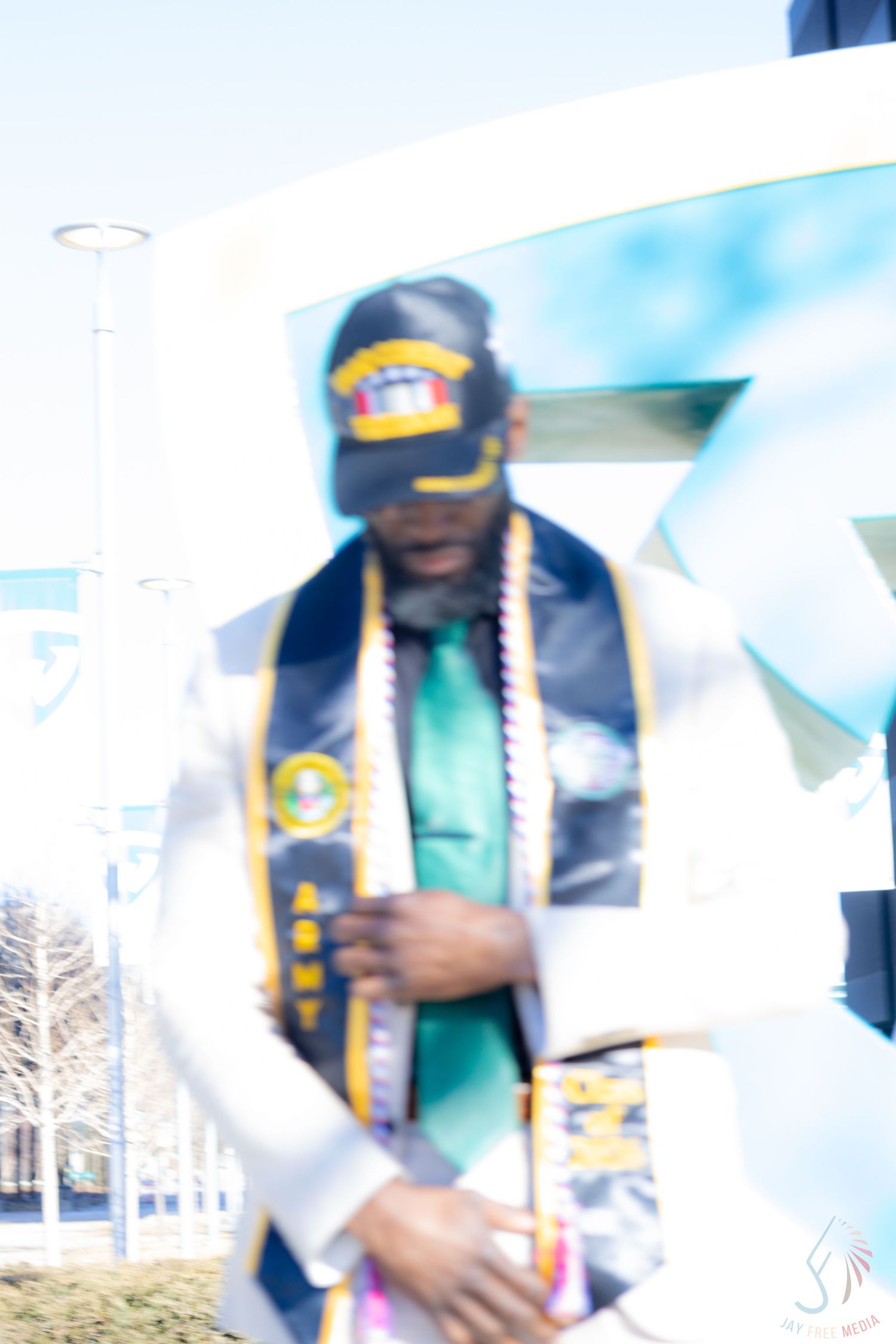 Army veteran graduate poses proudly in military cap and ARMY stole with graduation regalia outdoors.