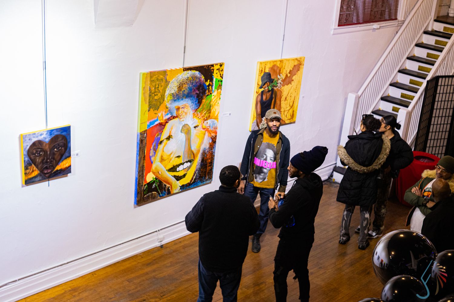 Overhead view of visitors admiring colorful paintings displayed on white gallery walls.