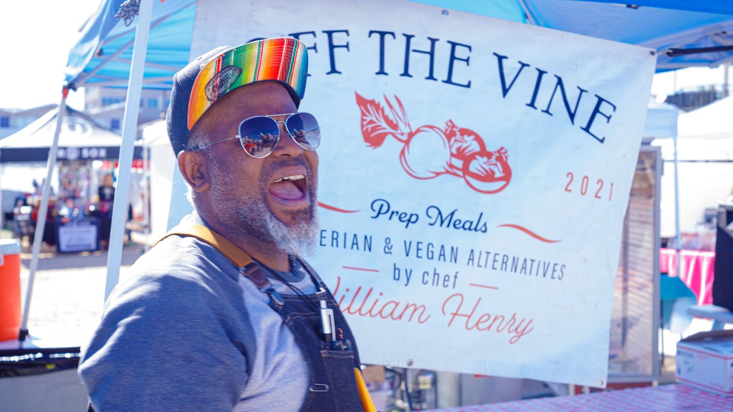 Chef William Henry smiling at Off The Vine vegan meal prep stand at outdoor festival.