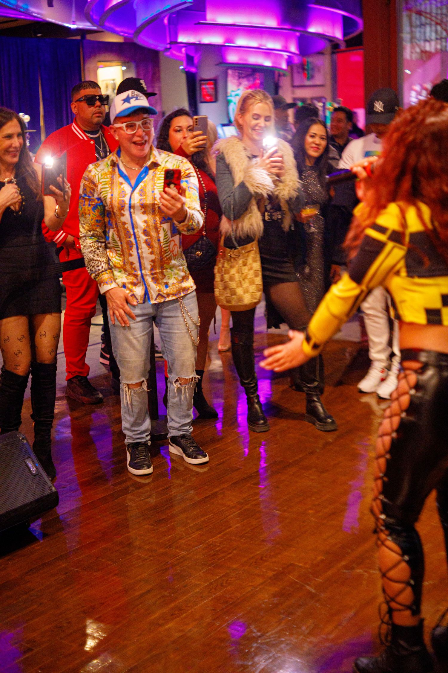 Crowd filming live performance at colorful nightclub event with performer on stage.