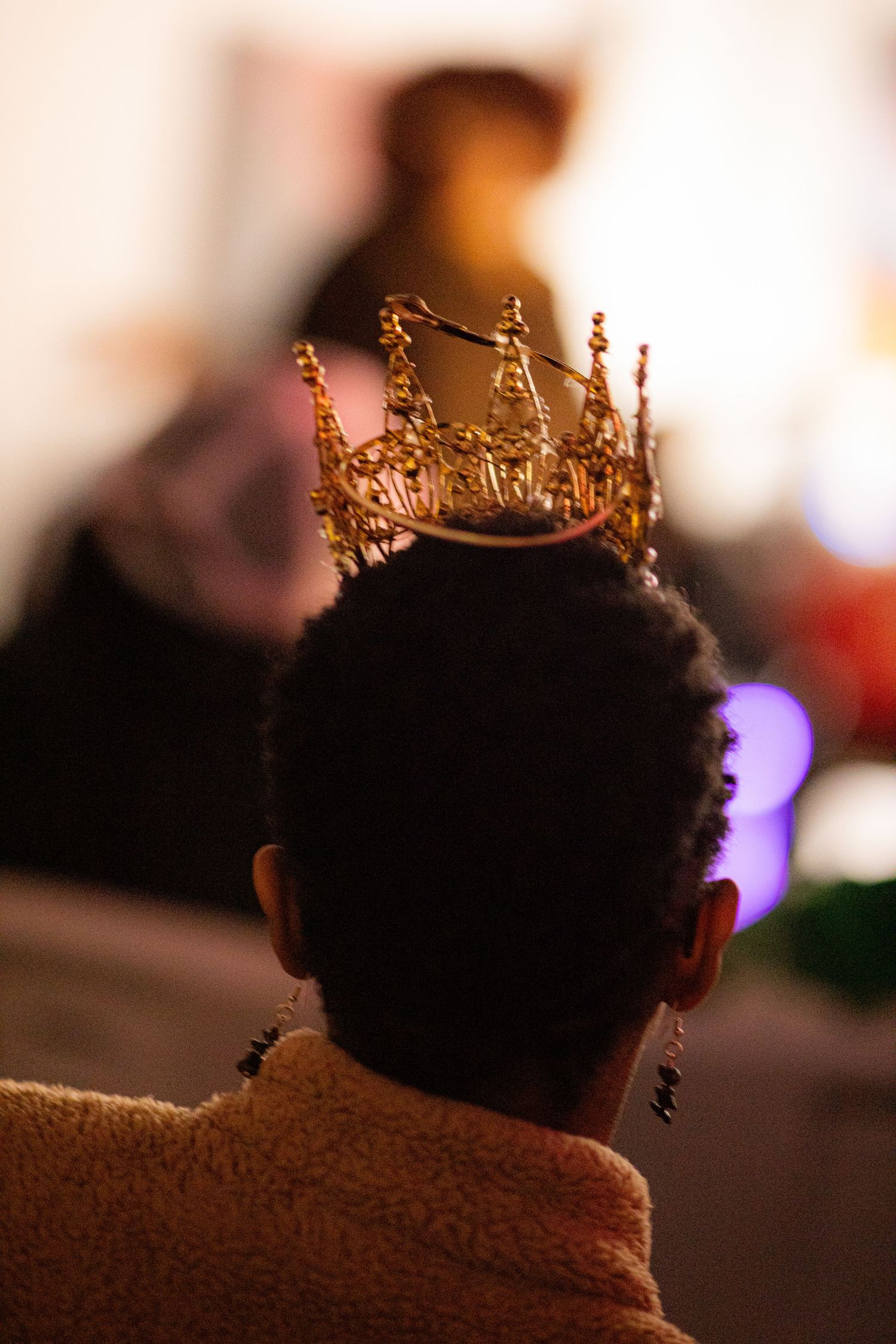 Person wearing an ornate gold crown seen from behind in a warmly lit room.