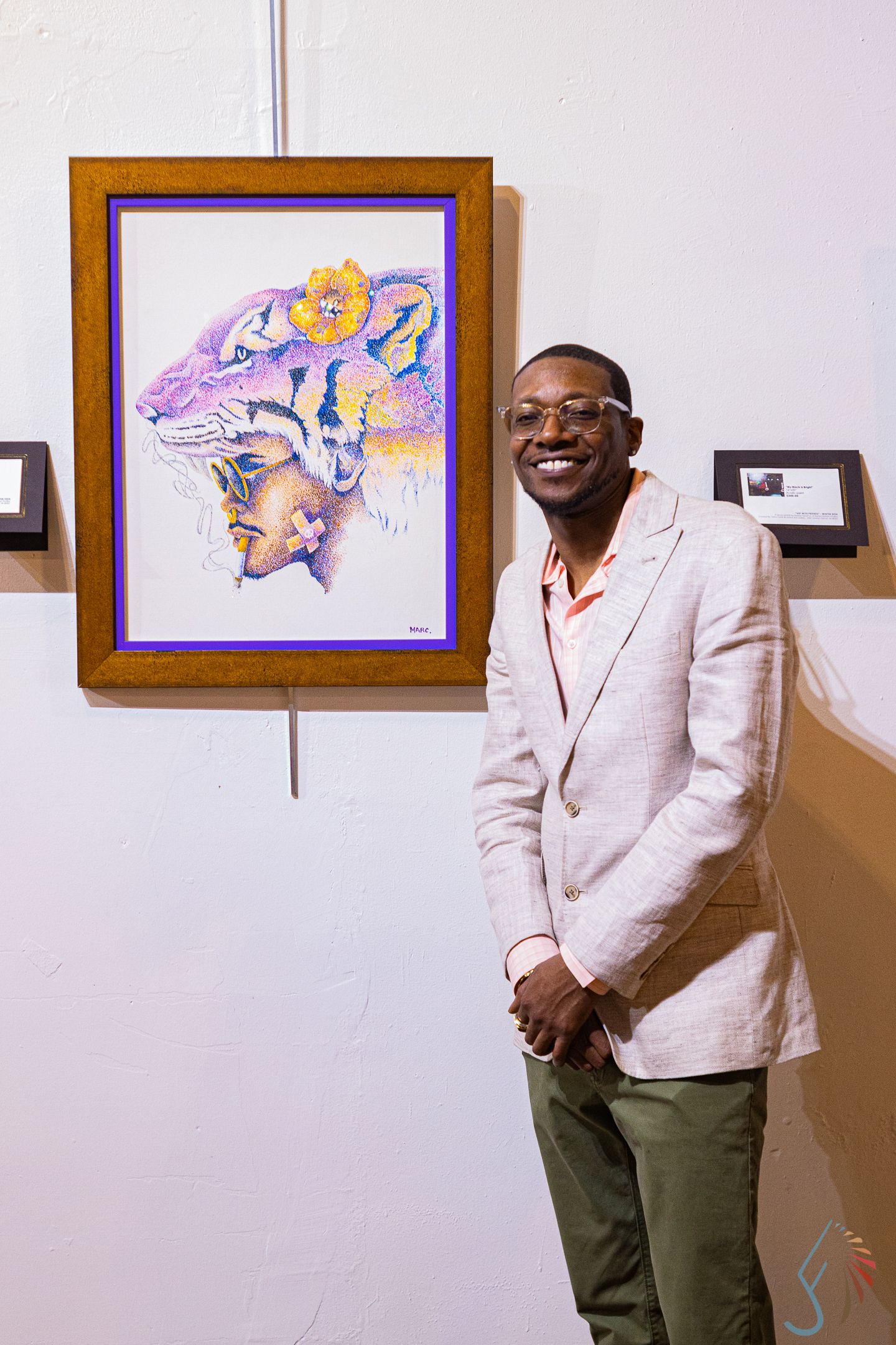 Smiling man in pink blazer standing beside colorful tiger artwork at an art gallery.
