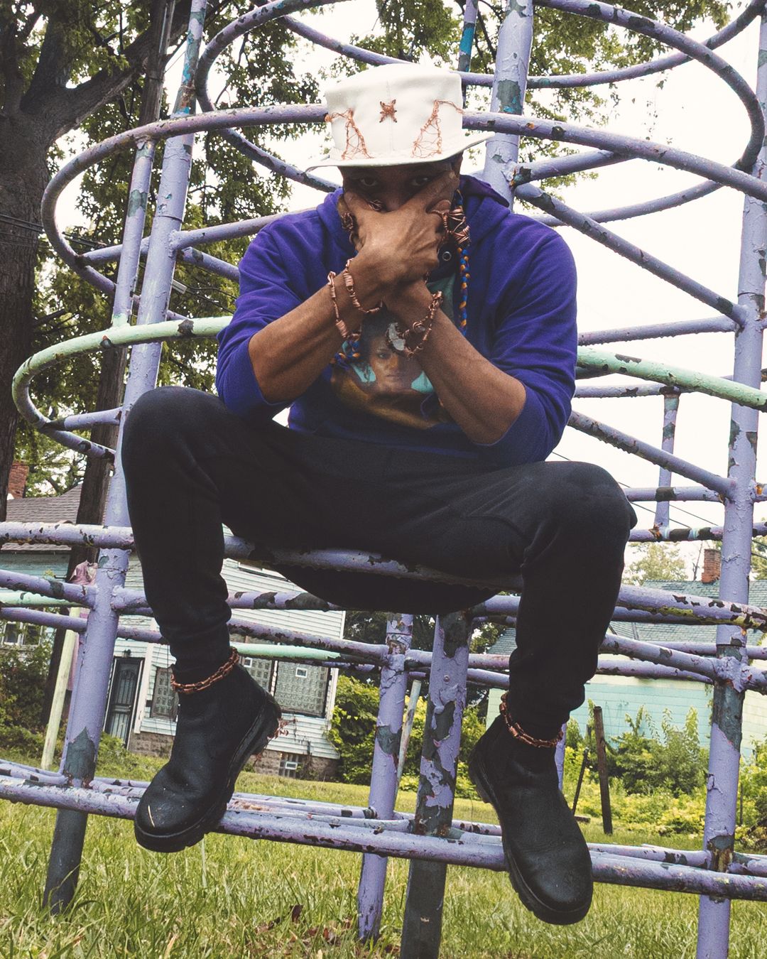 Jason Freeman in purple sweater and white hat sits on playground climbing structure outdoors.