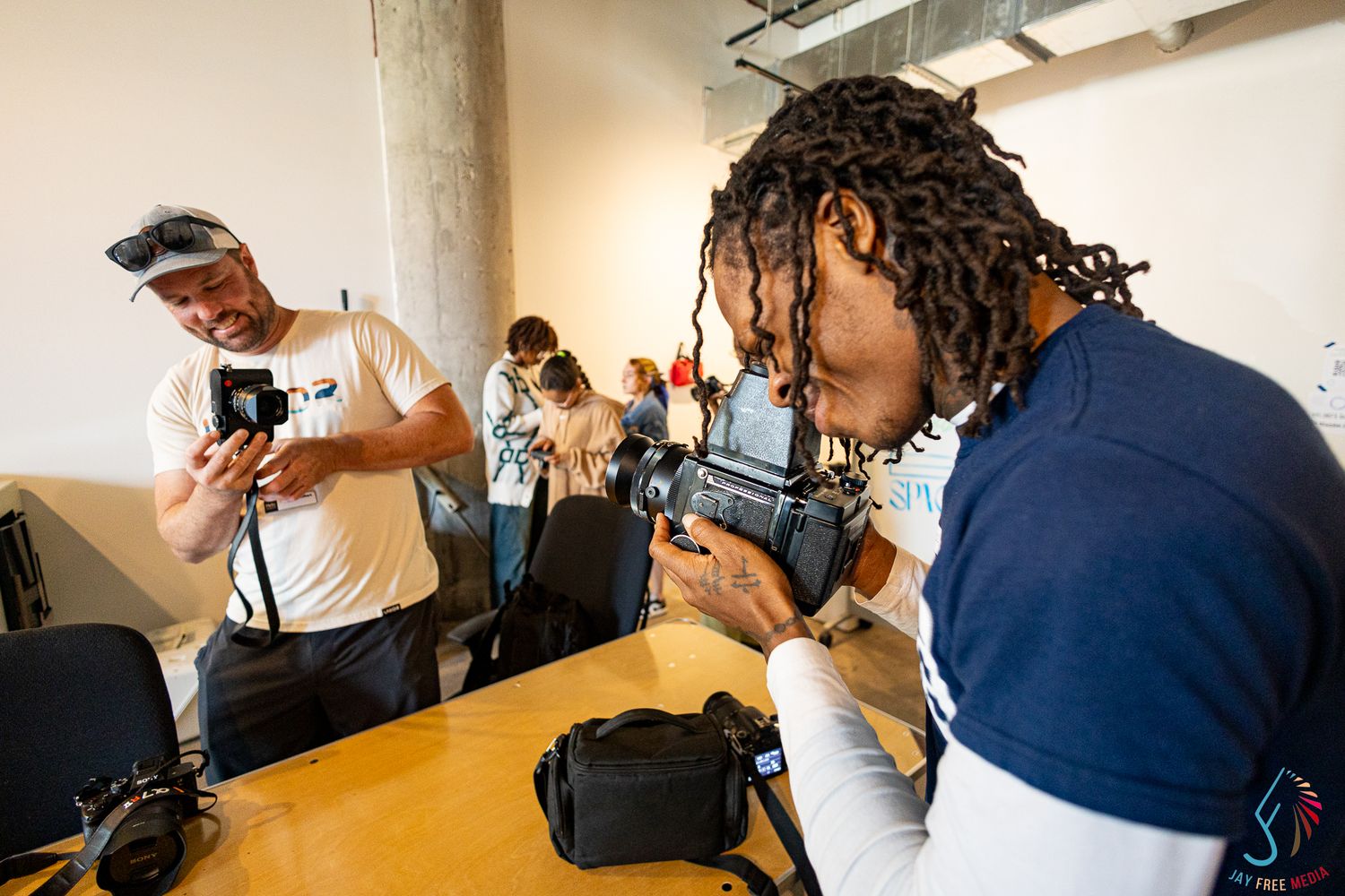 Students learning photography, examining cameras in a bright classroom workshop setting.