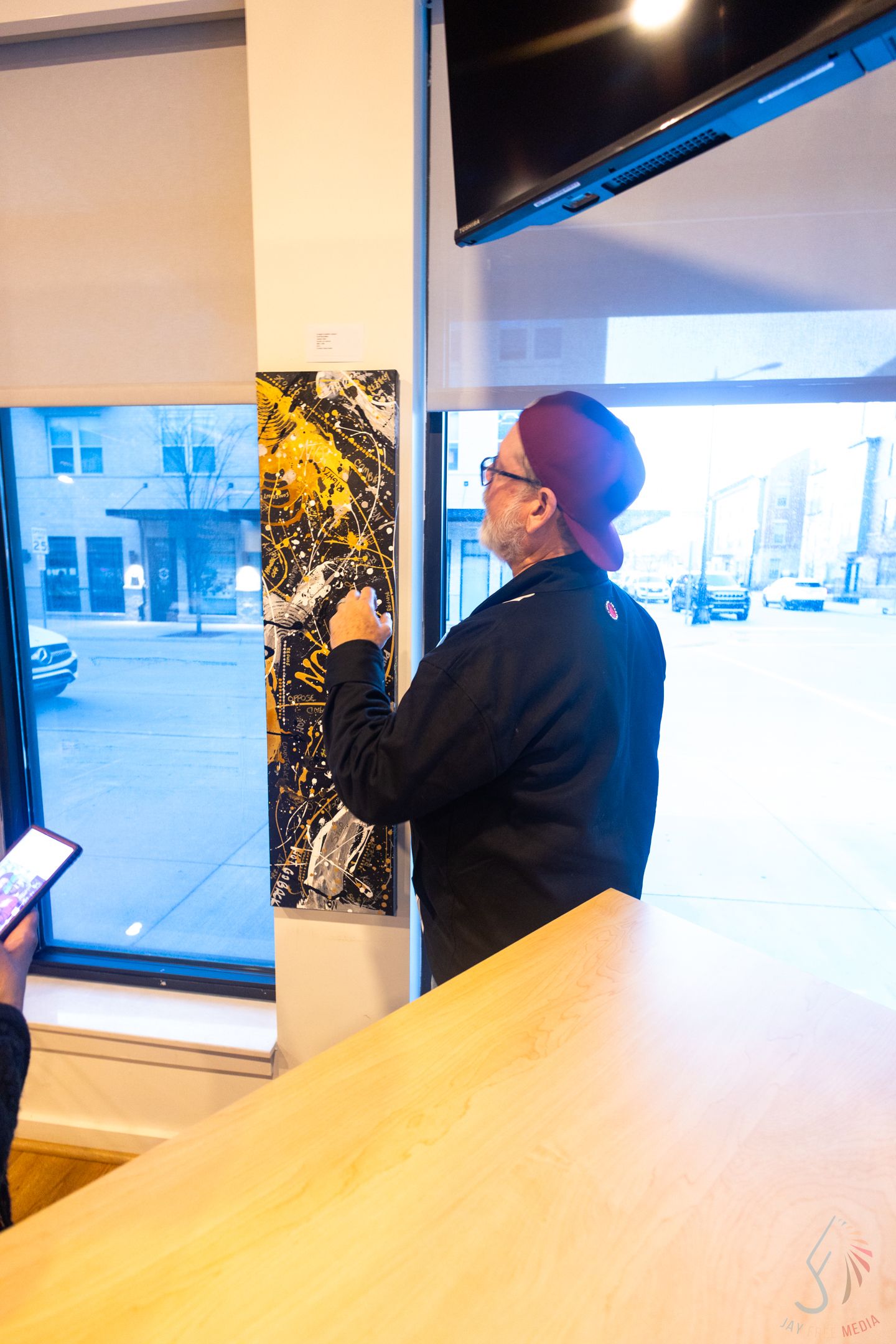 Artist hanging black and yellow abstract painting on white wall in modern gallery space with street view windows.