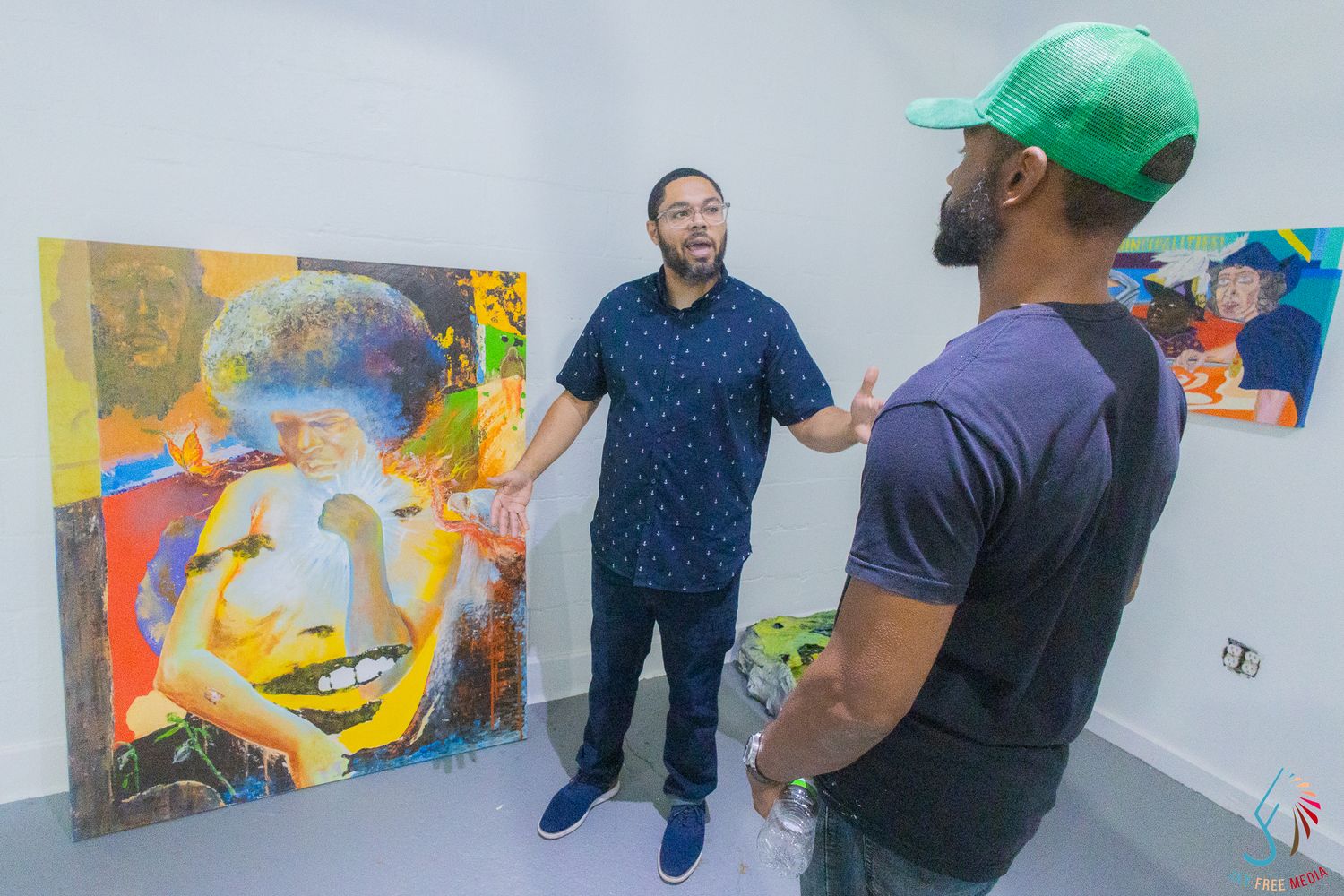 Two men discuss colorful portrait paintings in a bright art gallery setting.