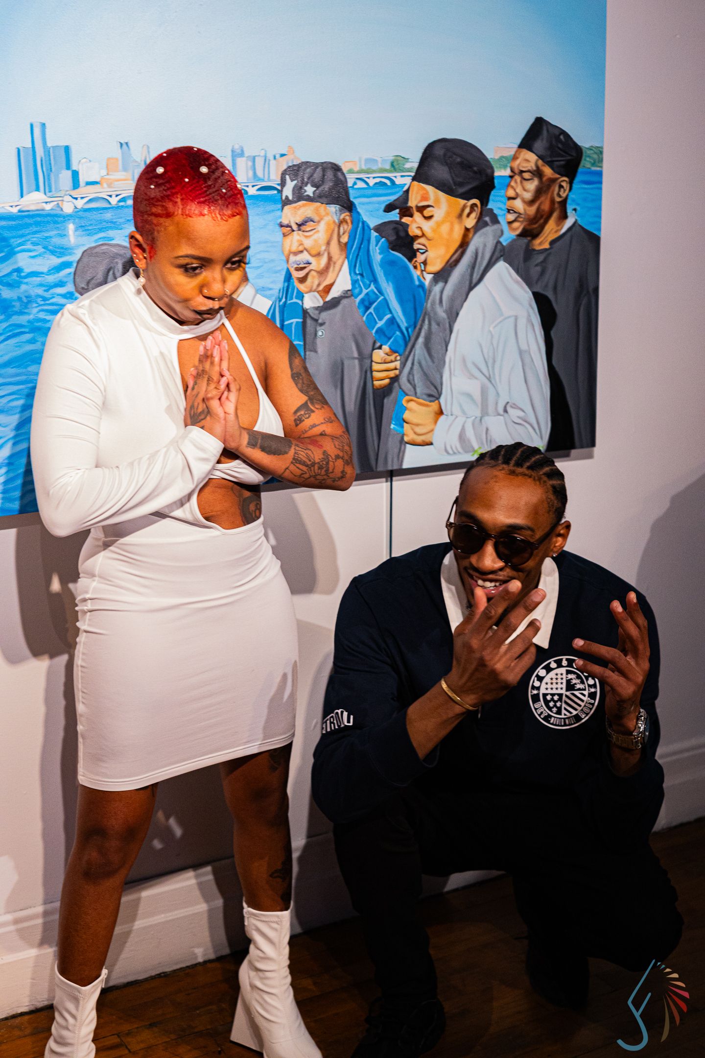 Two people posing playfully in front of a colorful urban painting at an art gallery event.