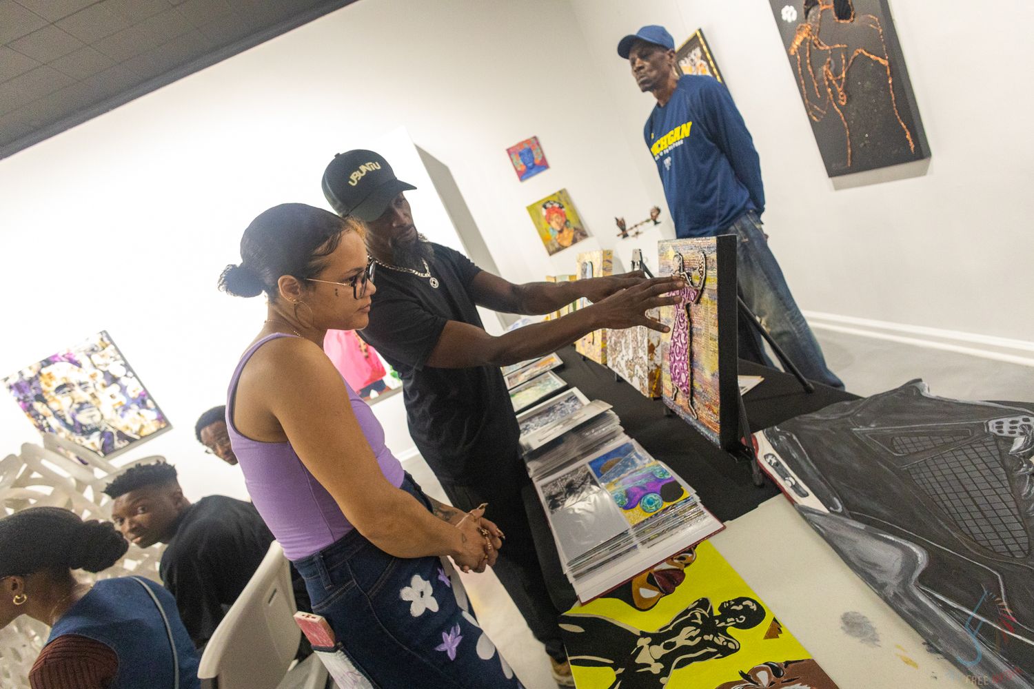 People browsing artwork and merchandise at an indoor art gallery event with colorful paintings displayed on walls.