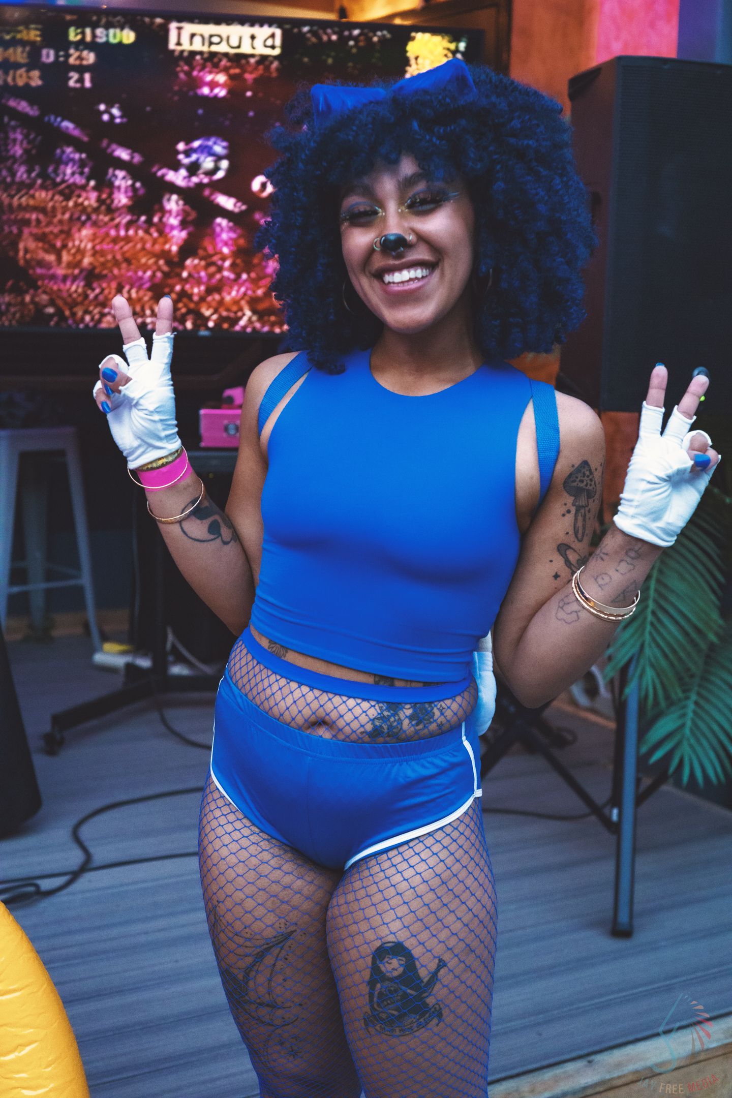 Person in bright blue outfit and fishnet stockings posing at a nightclub event.