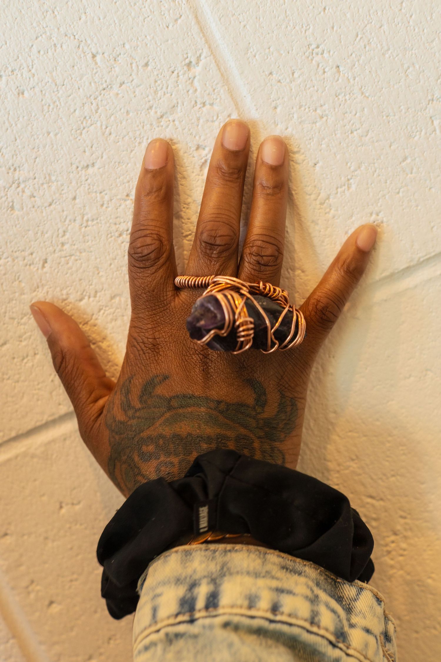 Close-up of hands wearing multiple decorative rings against a textured white wall.