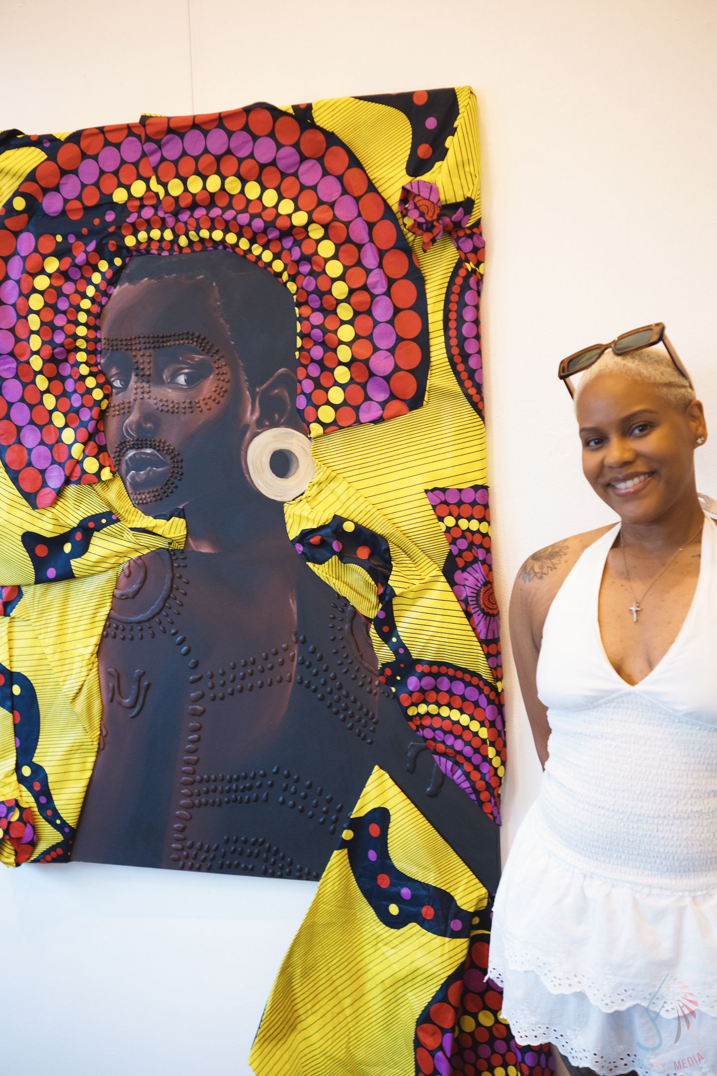 Woman smiling beside vibrant African-inspired textile portrait artwork in gallery.