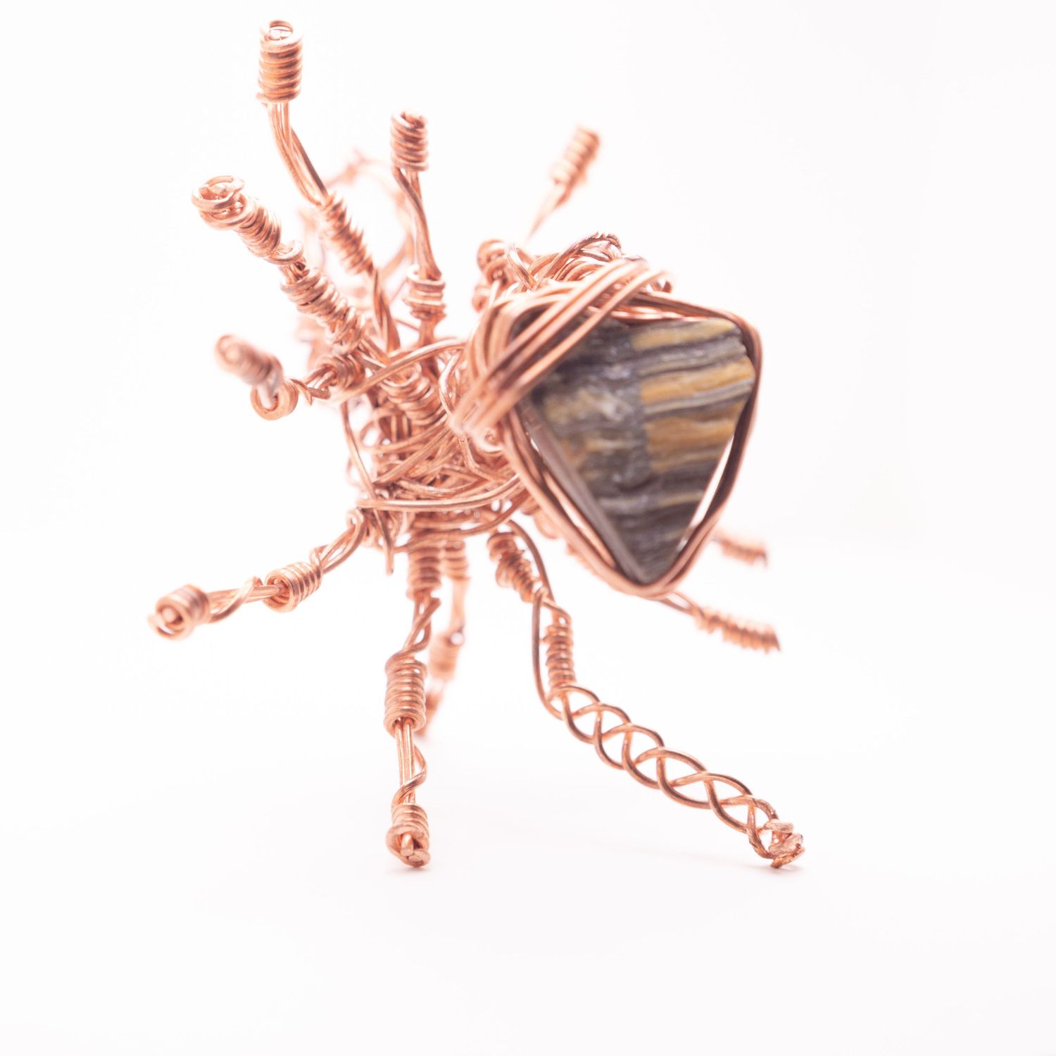 Copper wire wrapped sun-shaped brooch featuring a central tiger eye gemstone with radiating twisted wire rays.