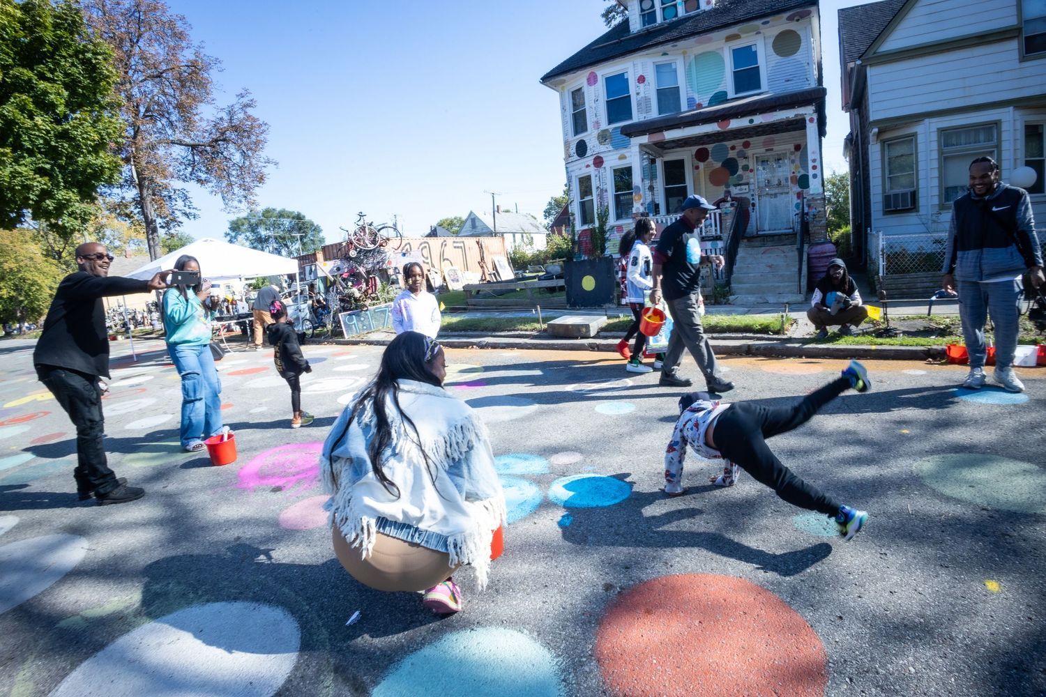 Community members painting colorful street art murals on a city road during an outdoor neighborhood beautification event.