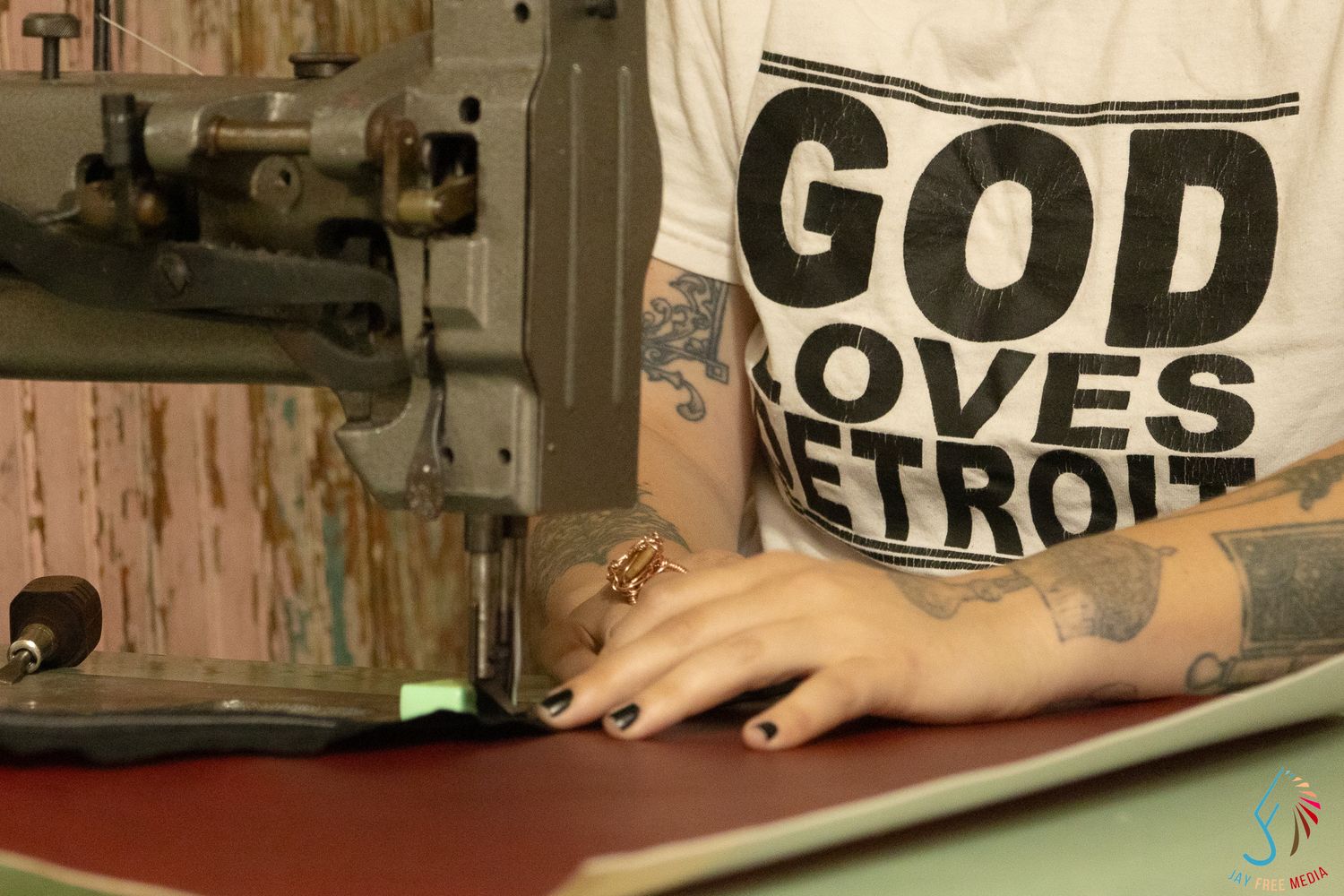 Tattooed woman wearing a God Loves Detroit shirt working at an industrial sewing machine.