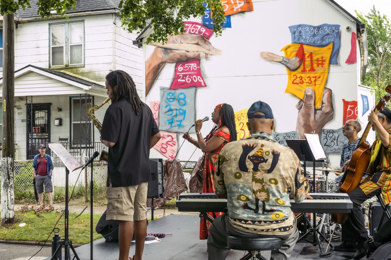 Outdoor jazz band performs in front of a colorful mural at a neighborhood street festival on a sunny day.