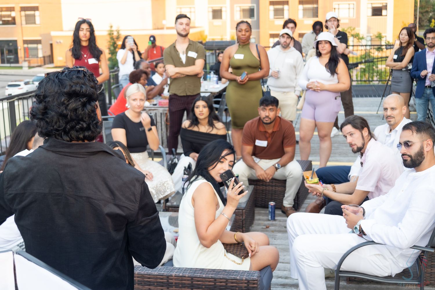 Diverse group of people gathered on rooftop patio listening to speaker at social networking event.