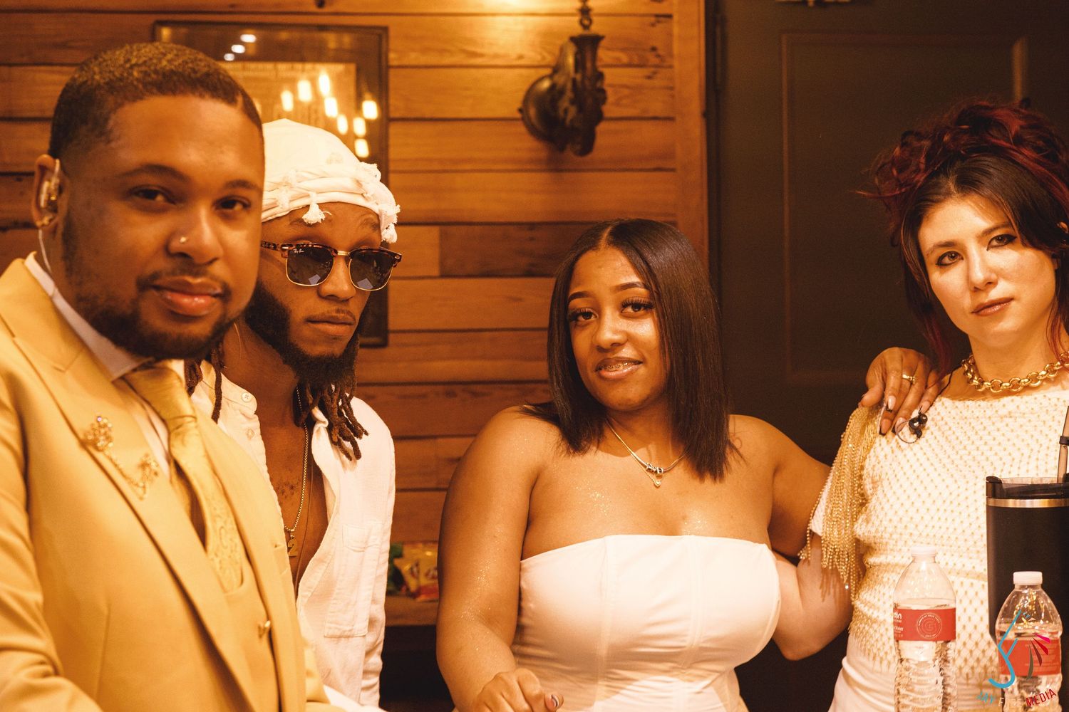 Four people posing together indoors at a social gathering, dressed in elegant attire in a warmly lit setting.