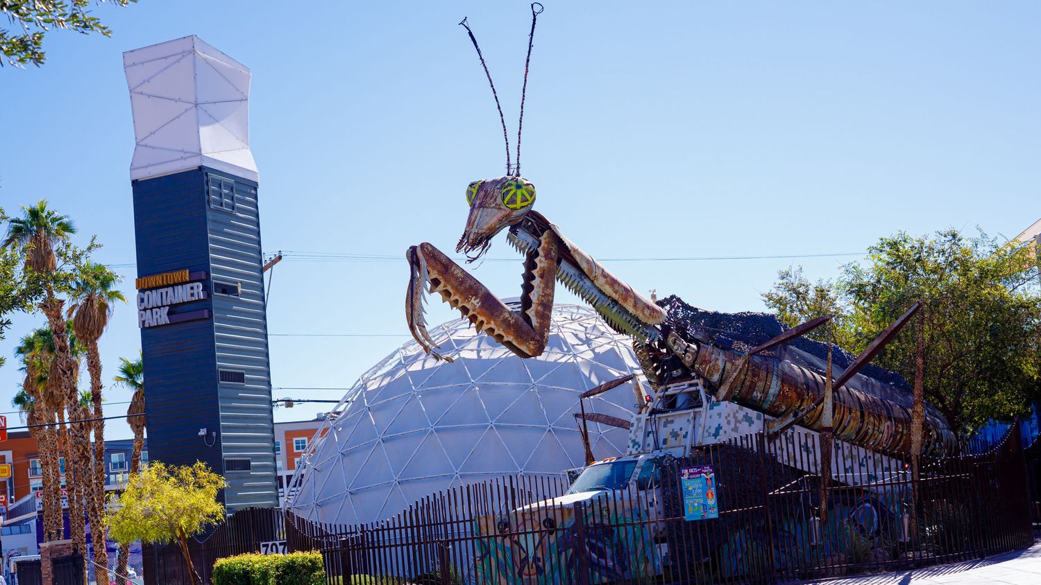 Giant praying mantis sculpture towering over a white dome building on the Las Vegas Strip under a clear blue sky.