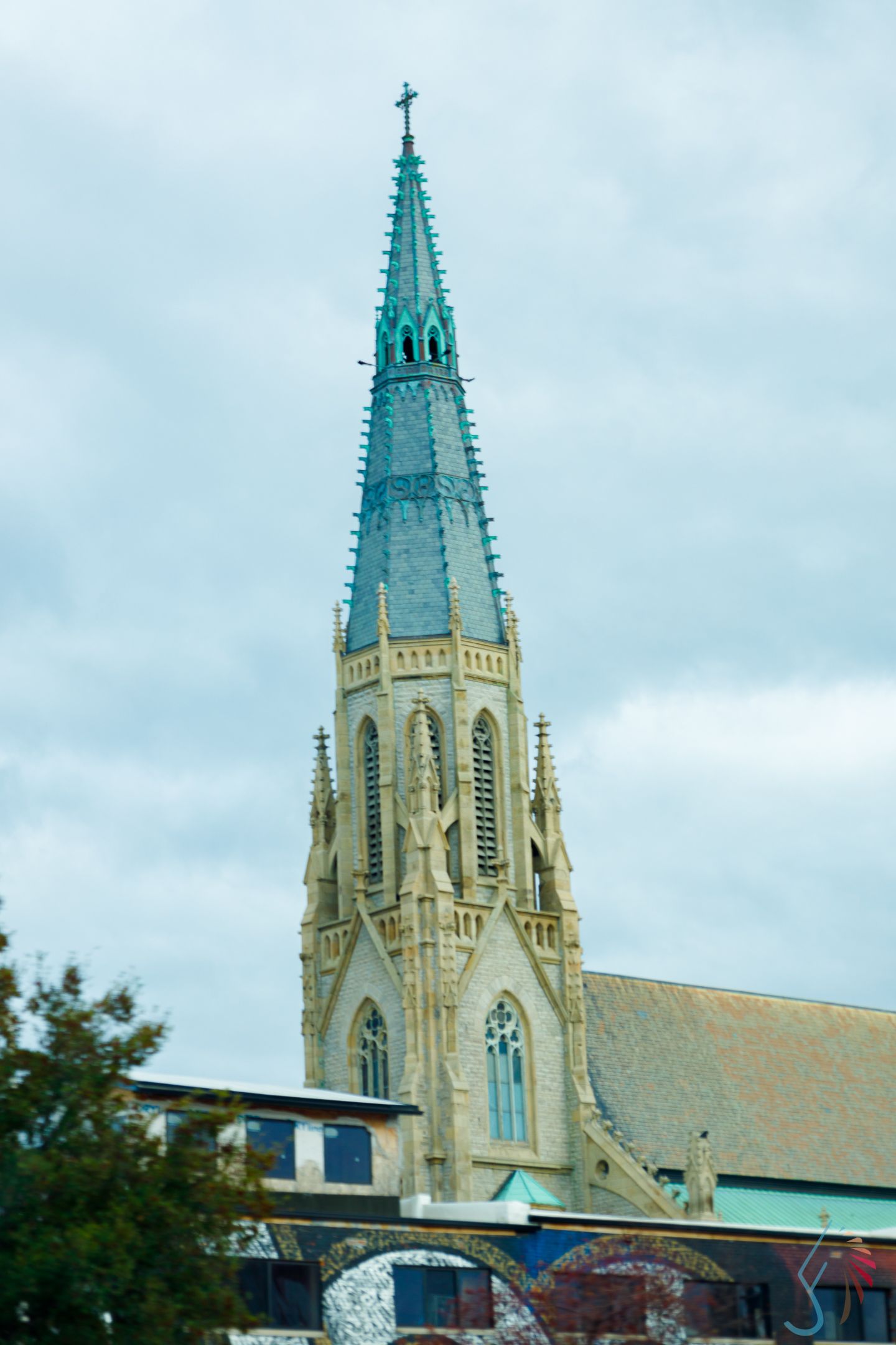 Gothic church steeple with green copper spire and cross against cloudy sky.