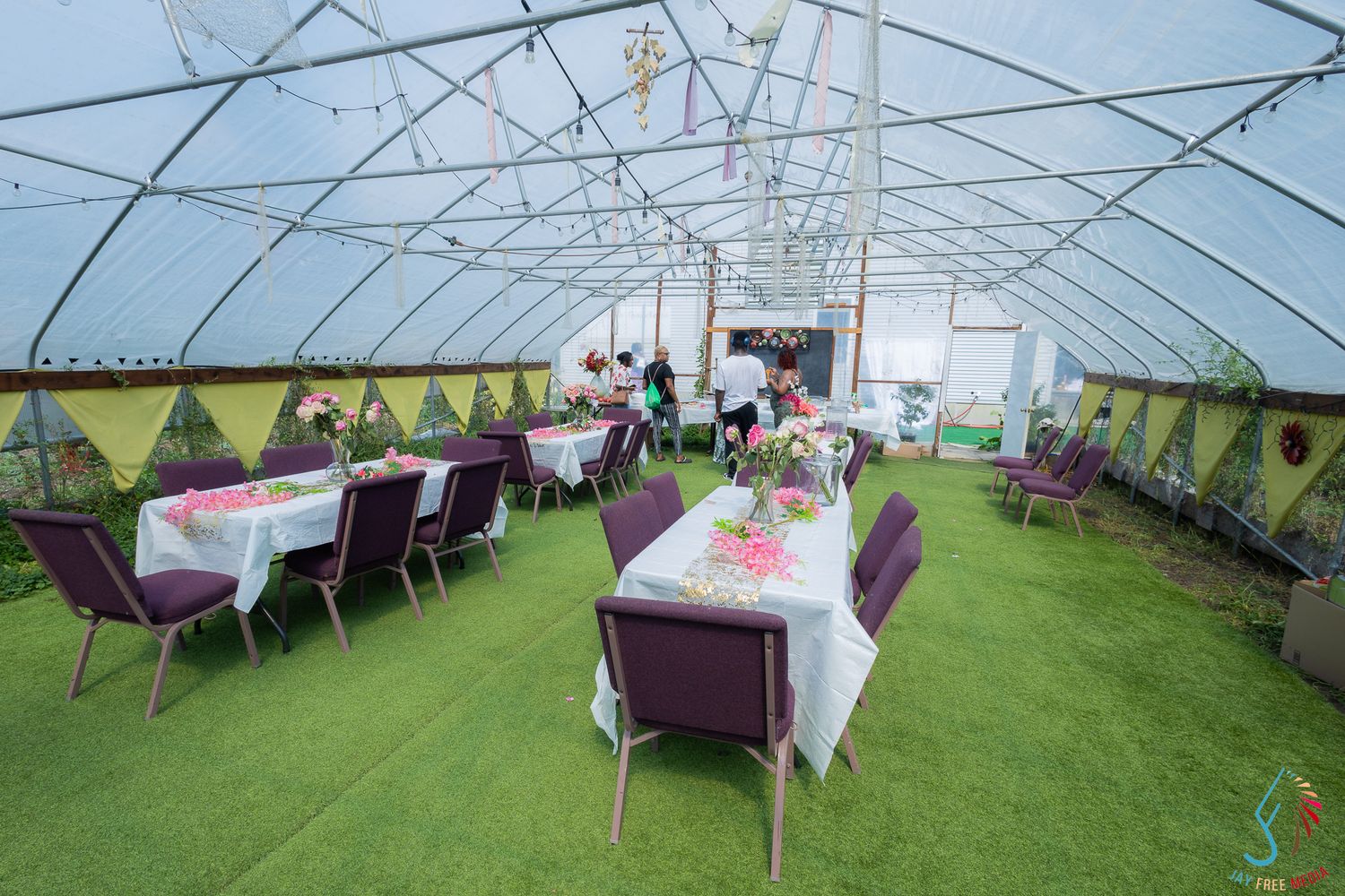 Elegant outdoor event tent with white-clothed tables, purple chairs, and string lights on green grass.