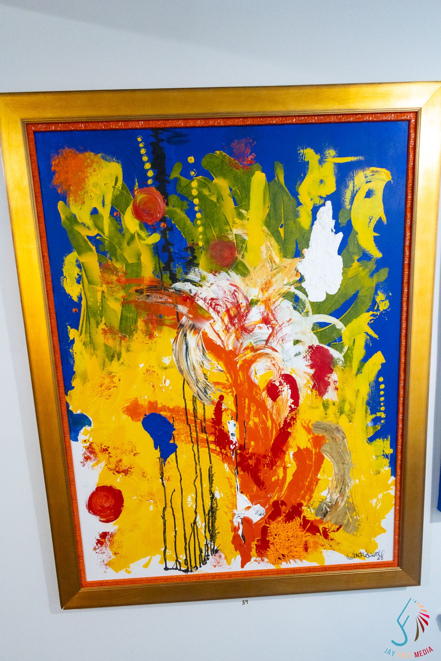 Vibrant abstract painting in gold frame featuring bold brushstrokes in blue, yellow, orange, red, and green colors.