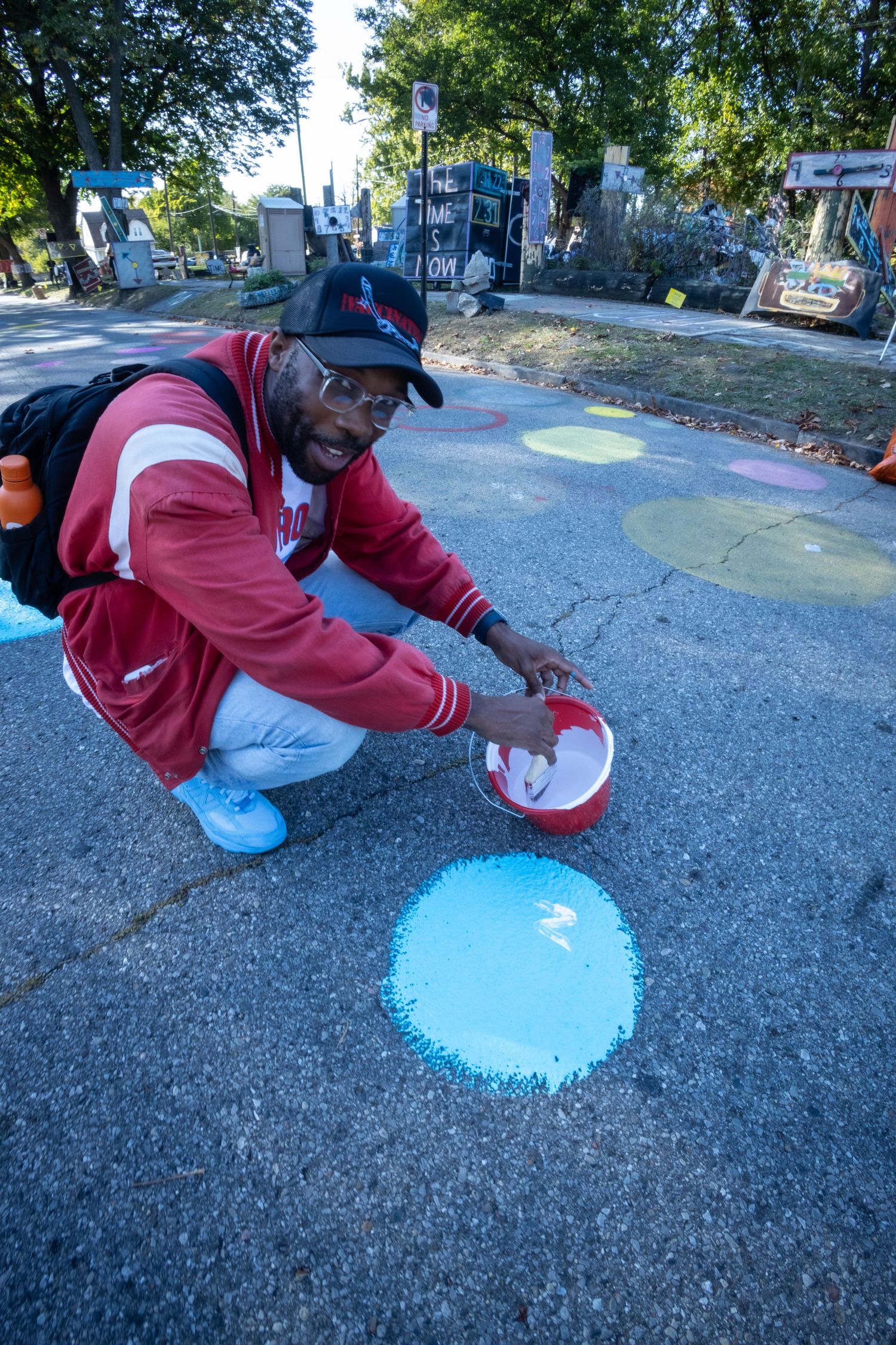 Man crouching on pavement painting a blue circle on the ground during an outdoor street art project.