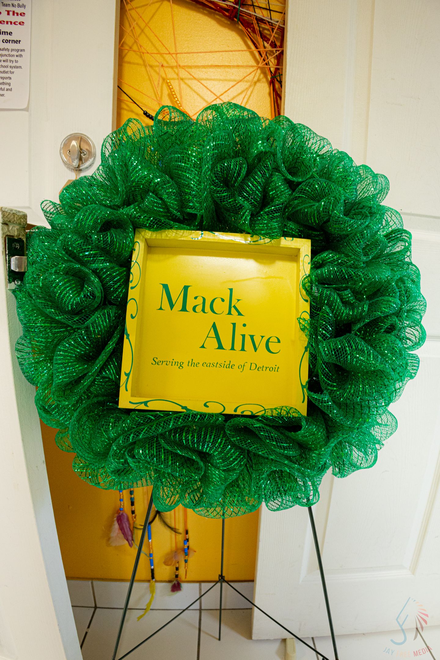Green mesh wreath with yellow Mack Alive sign serving the eastside of Detroit displayed on a metal stand.