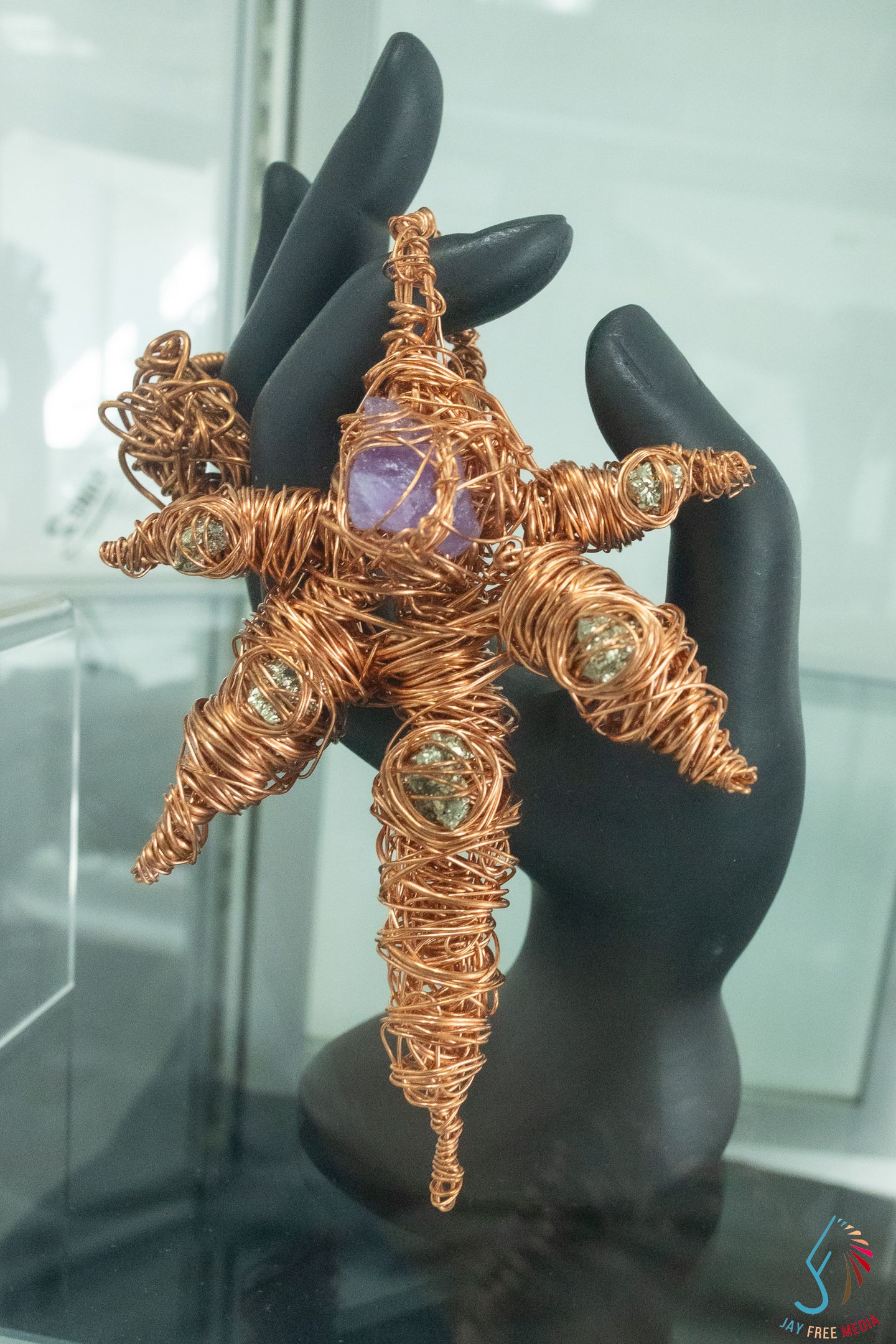 Copper wire art starfish sculpture with gemstones held by black mannequin hands on display.