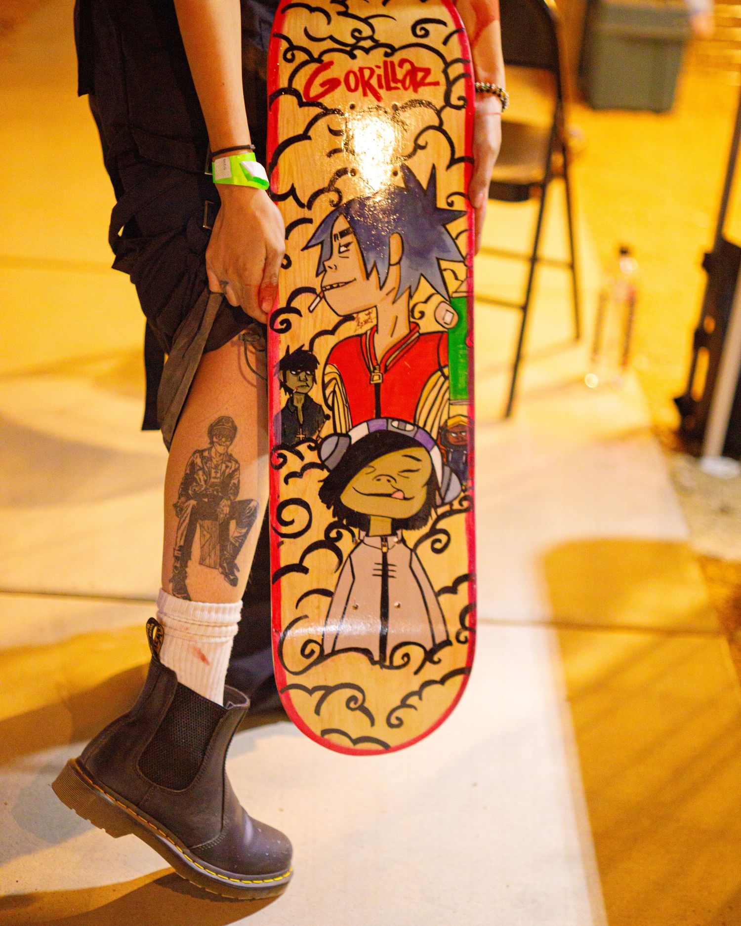 Person holding a Gorillaz-themed skateboard deck with cartoon artwork, wearing Dr. Martens boots.