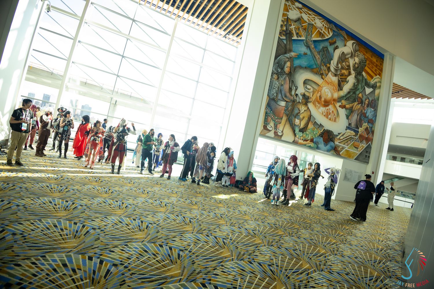 Cosplayers gather in large convention center lobby featuring colorful mural and patterned carpet floor.