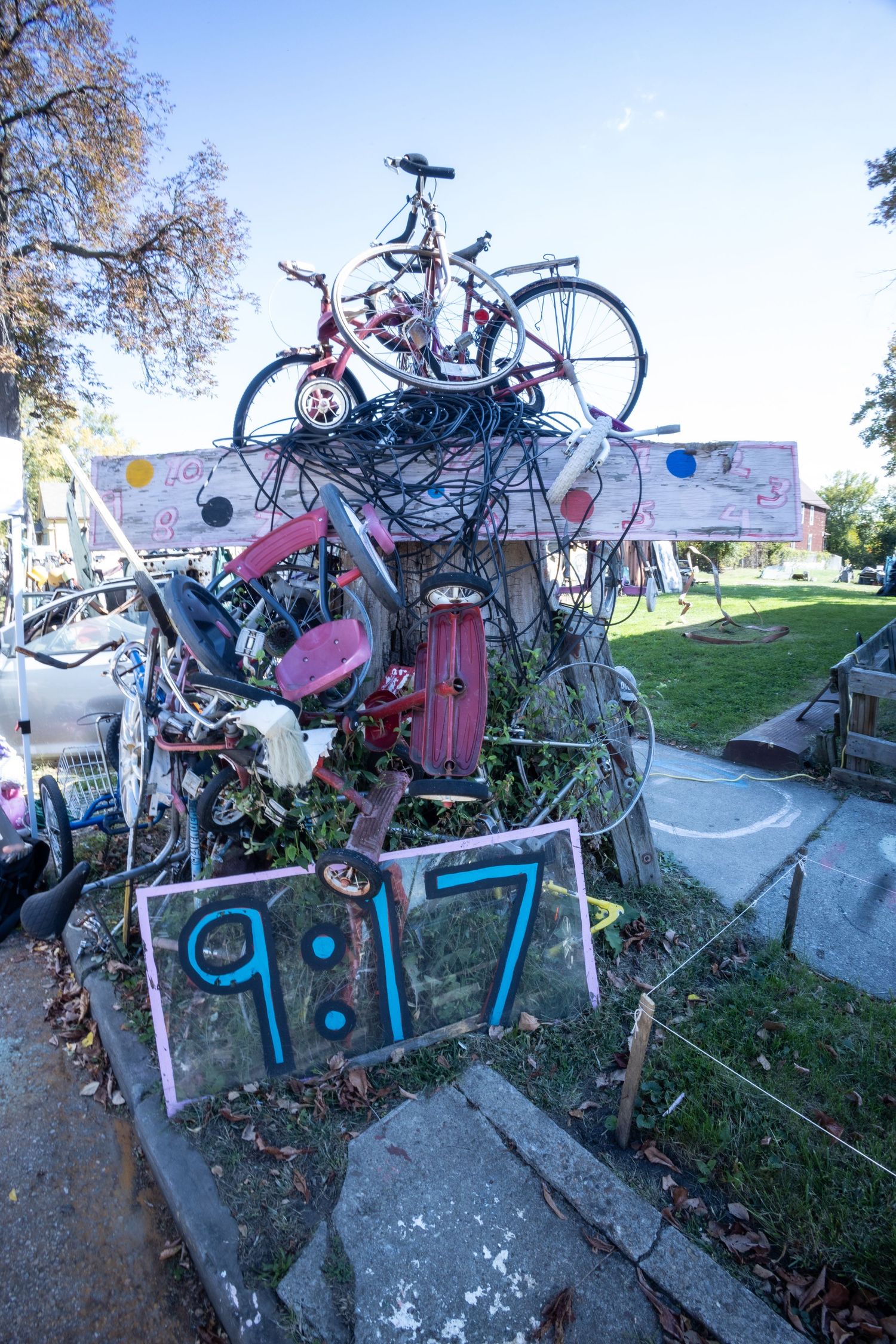 A sculptural assemblage of bicycles and metal with a sign reading 9:17 displayed outdoors.