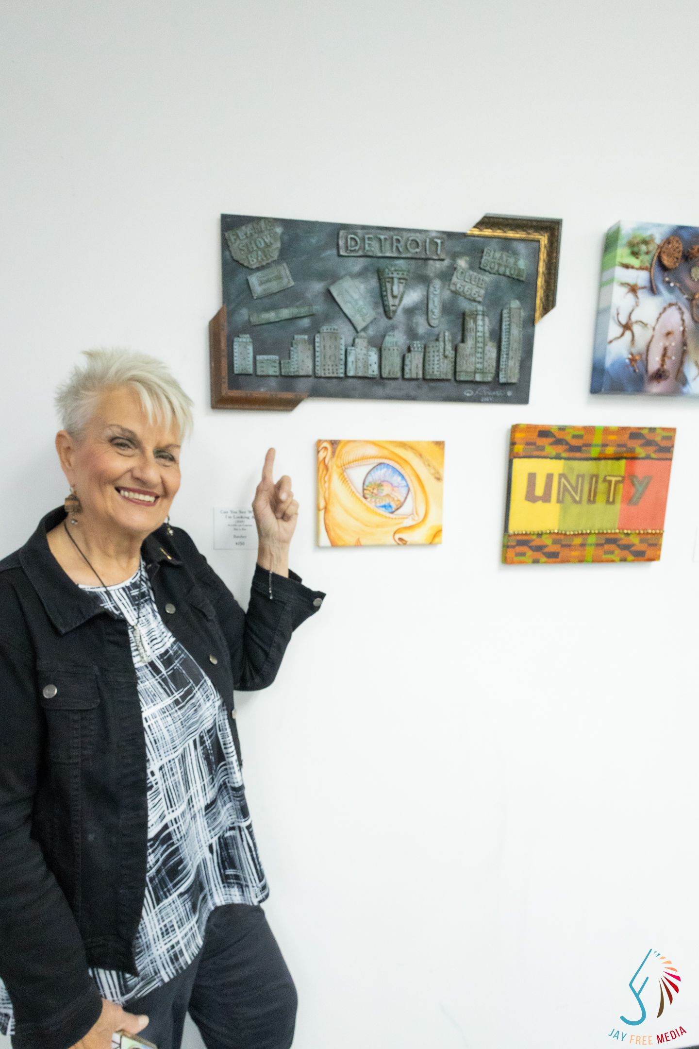 Woman smiling beside Detroit cityscape sculpture and Unity canvas at Black Rose Gallery of Art.