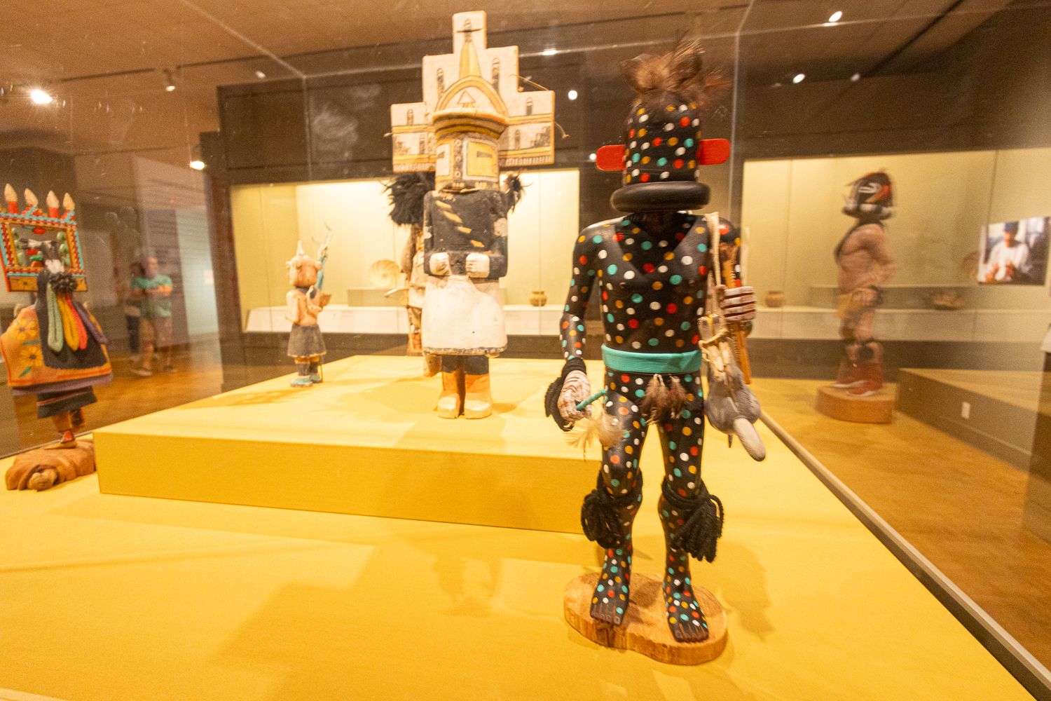 Colorful Native American Kachina doll figures on display in a museum exhibit with yellow platform.