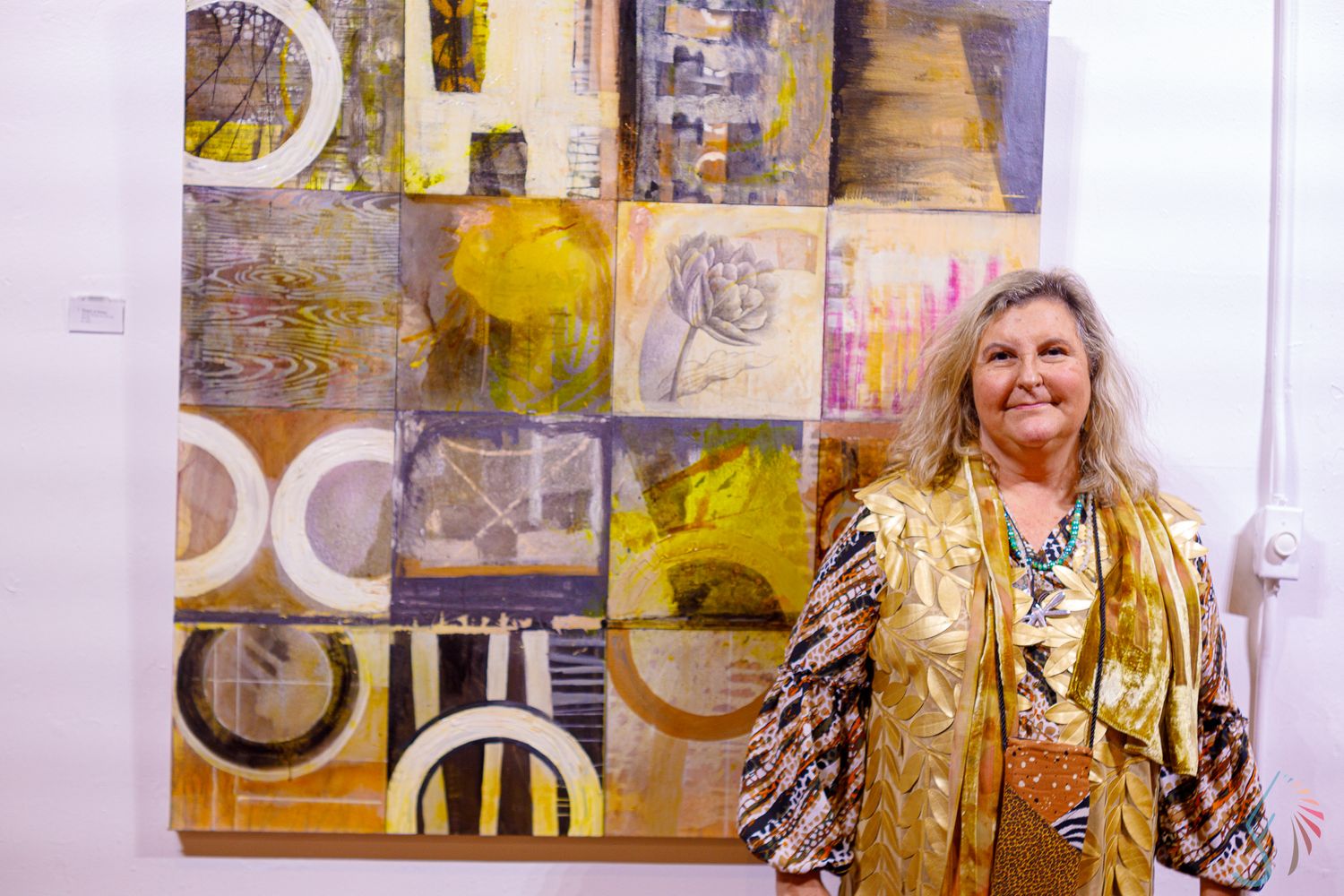 Woman smiling beside large yellow abstract artwork featuring geometric shapes and circles at an art gallery exhibition.