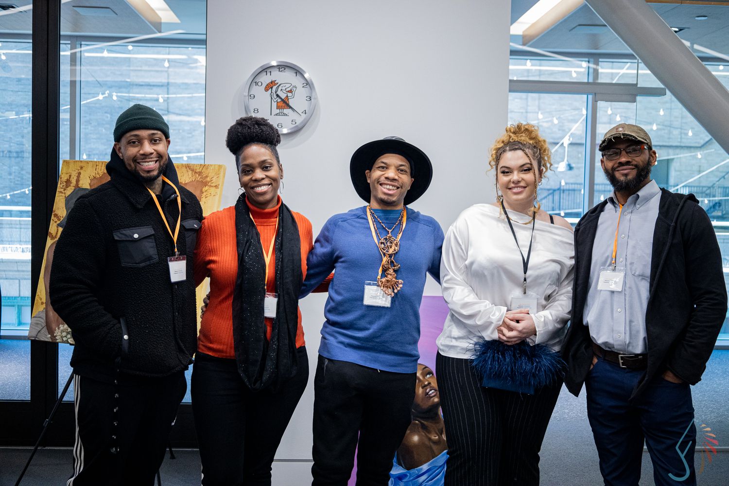 Five diverse professionals smile together for a group photo in a bright modern office space.