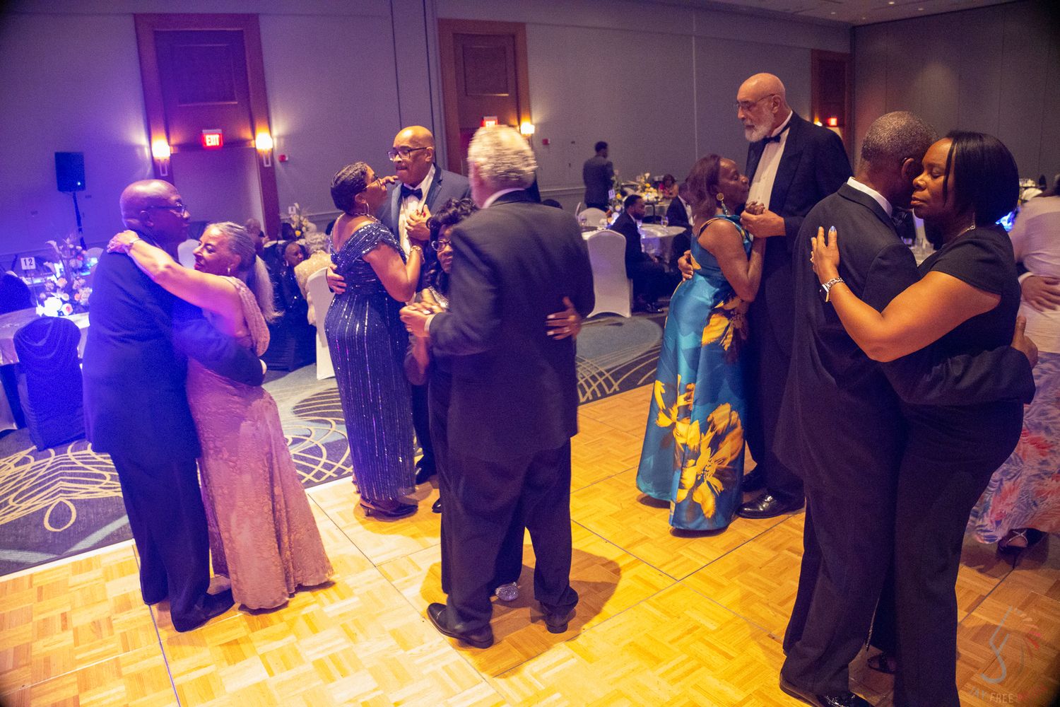 Couples dancing together at an elegant formal ballroom event with blue ambient lighting.